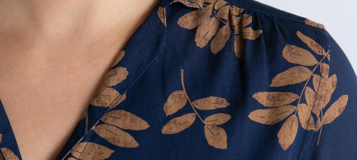 Close-up of a person wearing a dark blue shirt with a brown leaf pattern. The shirt has a collar, and only the lower part of the neck and upper chest are visible.