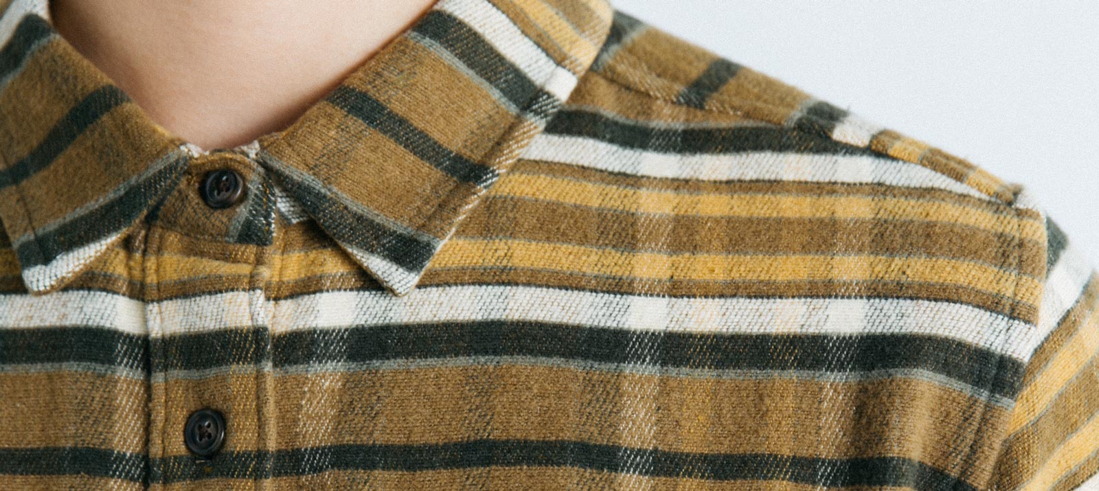 A close-up of a person wearing a buttoned-up, collared shirt with horizontal mustard yellow, white, and black stripes. Only the neck and upper chest are visible.