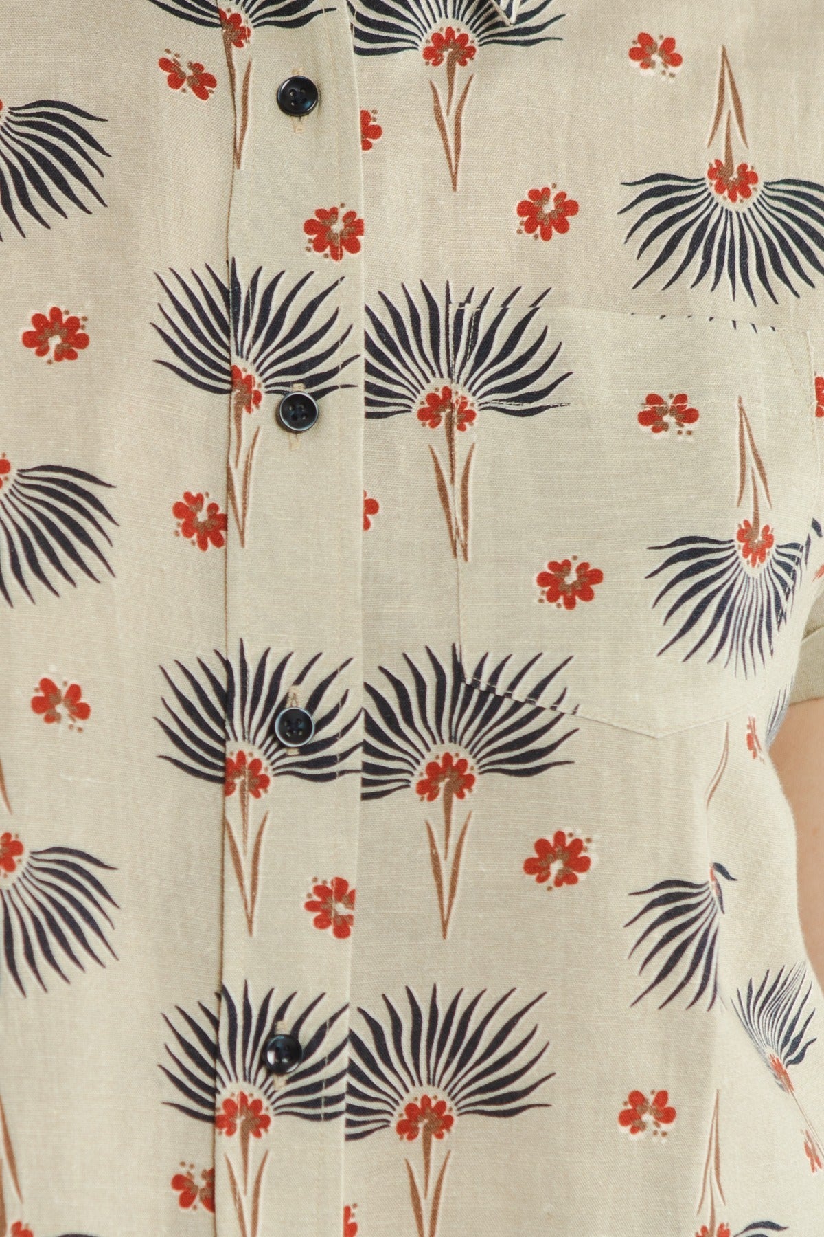 Close-up of the Bridge & Burn Bea Shirt / Aloha Floral: a beige short-sleeve button-down with black palm-like shapes, small red flowers, black buttons, and a visible right pocket.