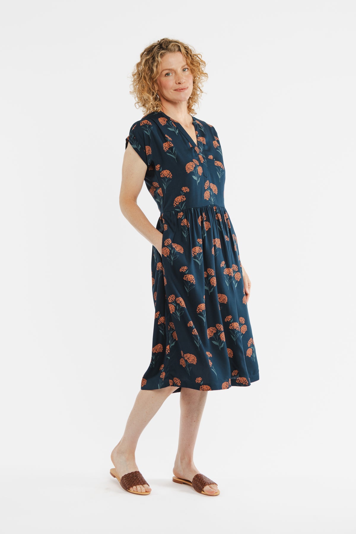 The Bridge & Burn Ira Dress / Wildflower is a navy blue knee-length modal pullover with short sleeves, a V-neckline, an elastic waist, and an orange and green floral print. Shown laid flat on a white background.