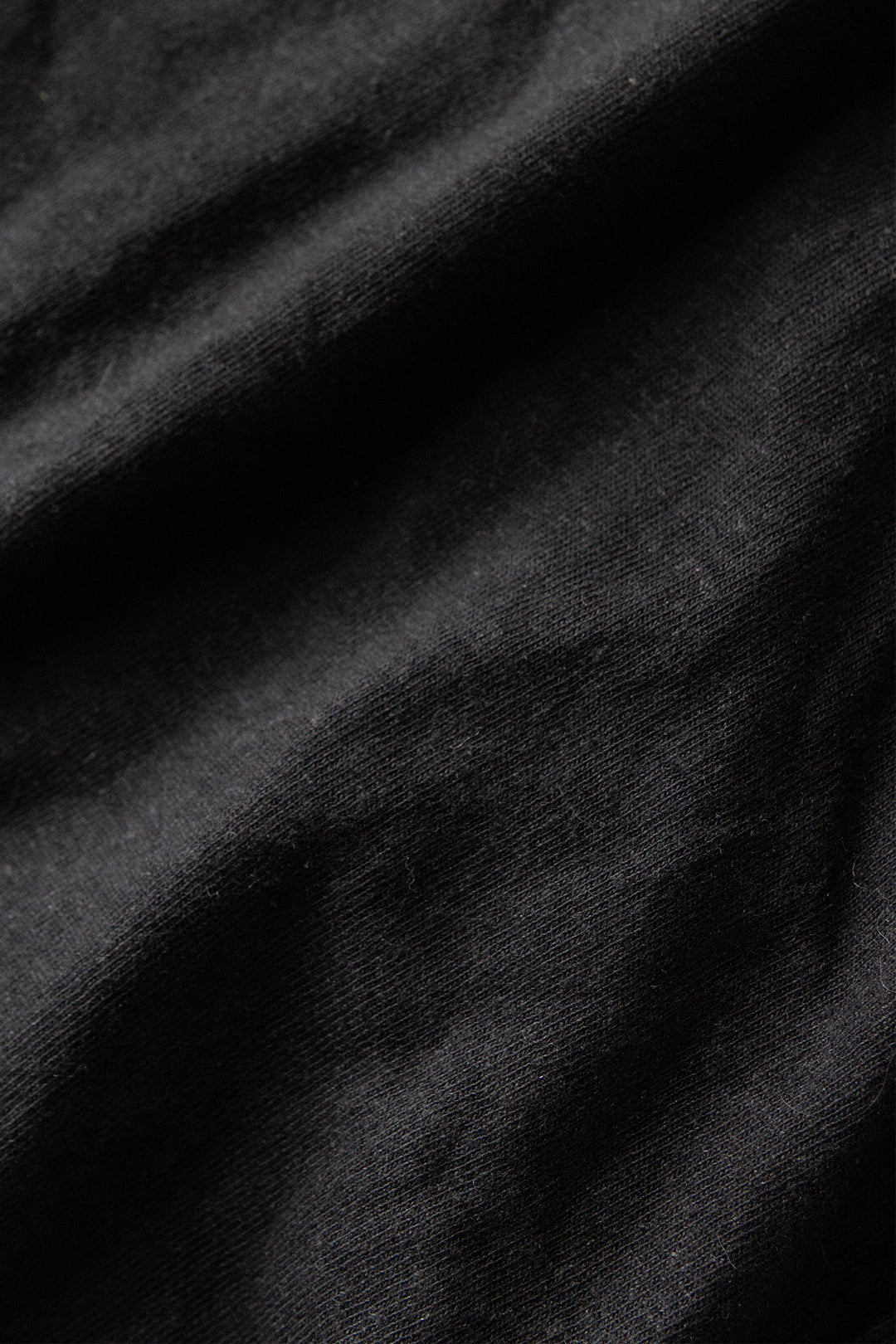 Close-up of black fabric with visible texture and subtle folds, highlighting the soft shadows and details of the Bridge & Burn Organic Hemp Pocket Tee in Washed Black, crafted for comfort, style, and sustainability.
