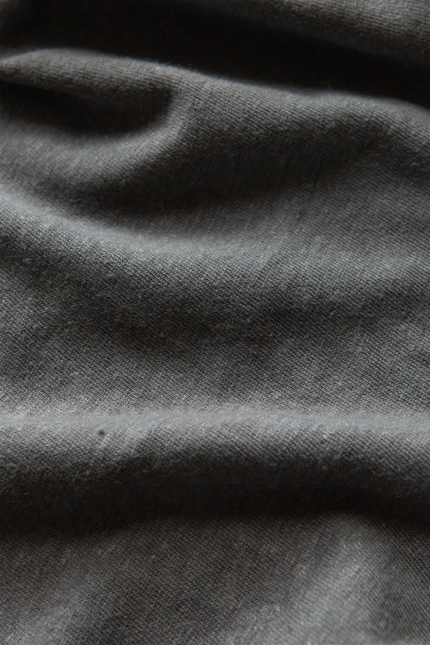 Close-up of the Organic Hemp Pocket Tee in Slate Grey by Bridge & Burn, highlighting its sustainable dark gray fabric with visible texture and soft, irregular folds and shadows.