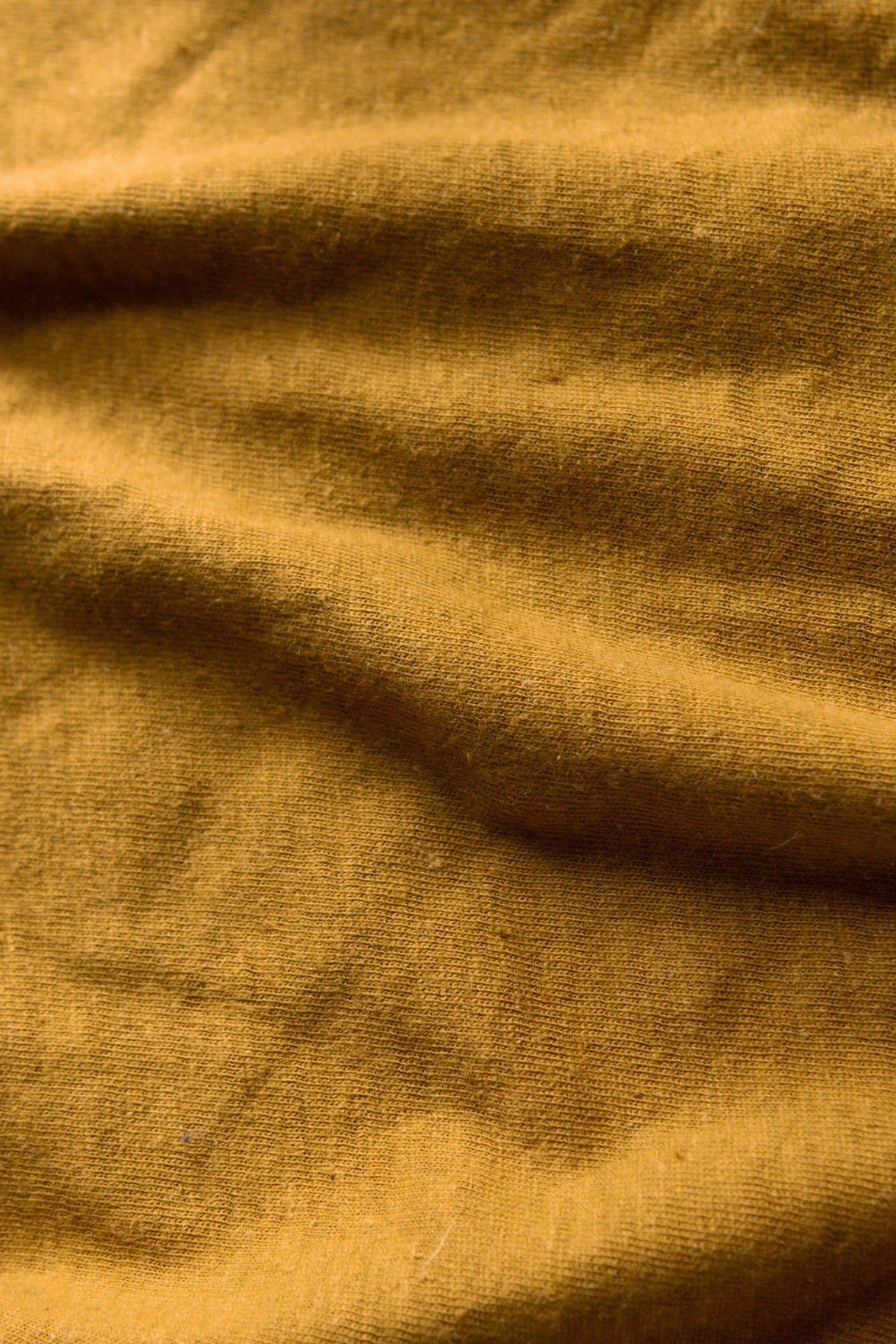A close-up of the Organic Hemp Pocket Tee in ochre by Bridge & Burn reveals its woven texture and soft folds—perfect for a sustainable t-shirt made from organic cotton and hemp.