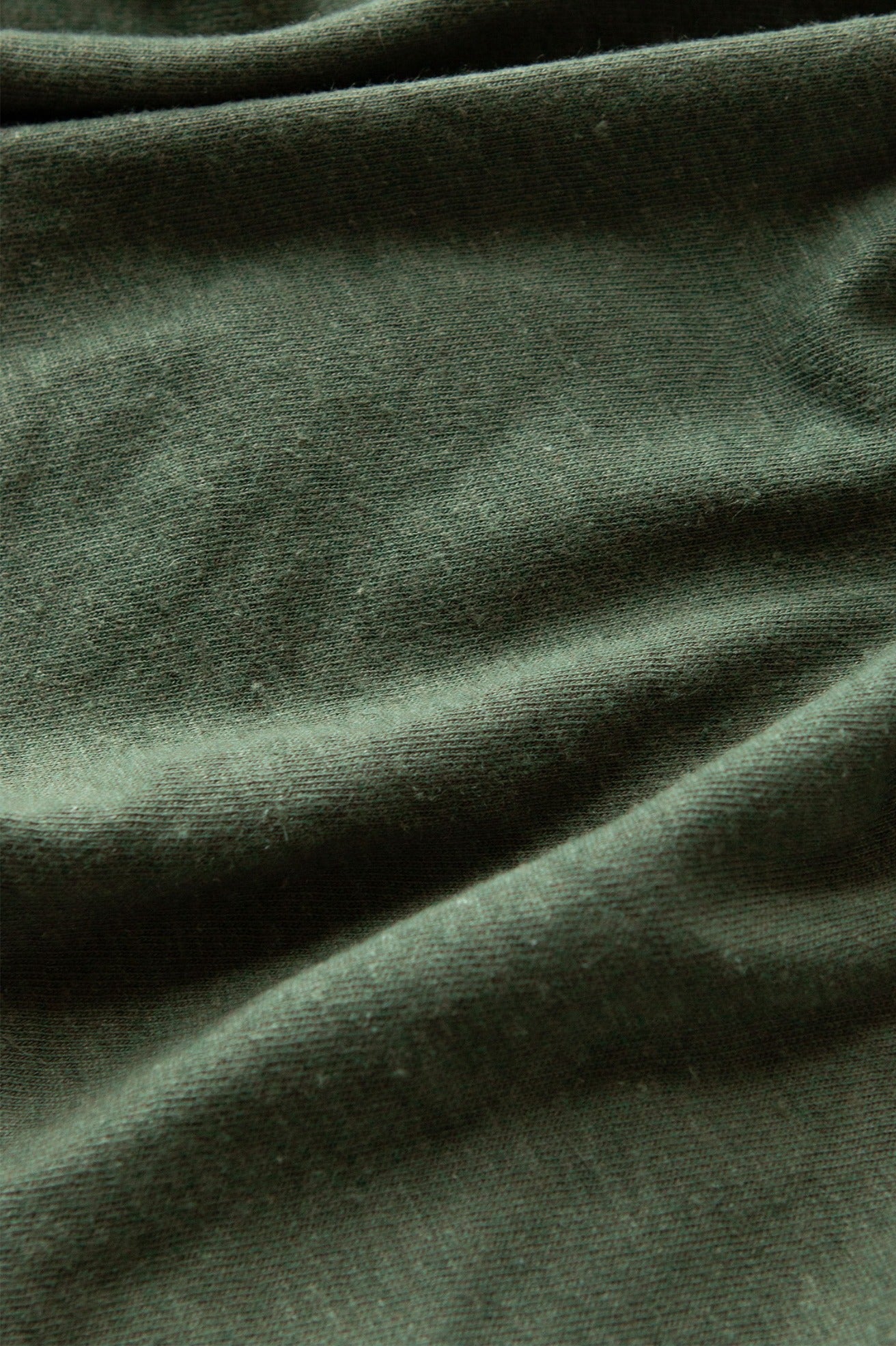 Close-up of the Bridge & Burn Organic Hemp Pocket Tee in Cypress, showing its dark green organic cotton-hemp fabric with a soft texture, gentle folds, and subtle shadows—highlighting this sustainable t-shirt’s quality.