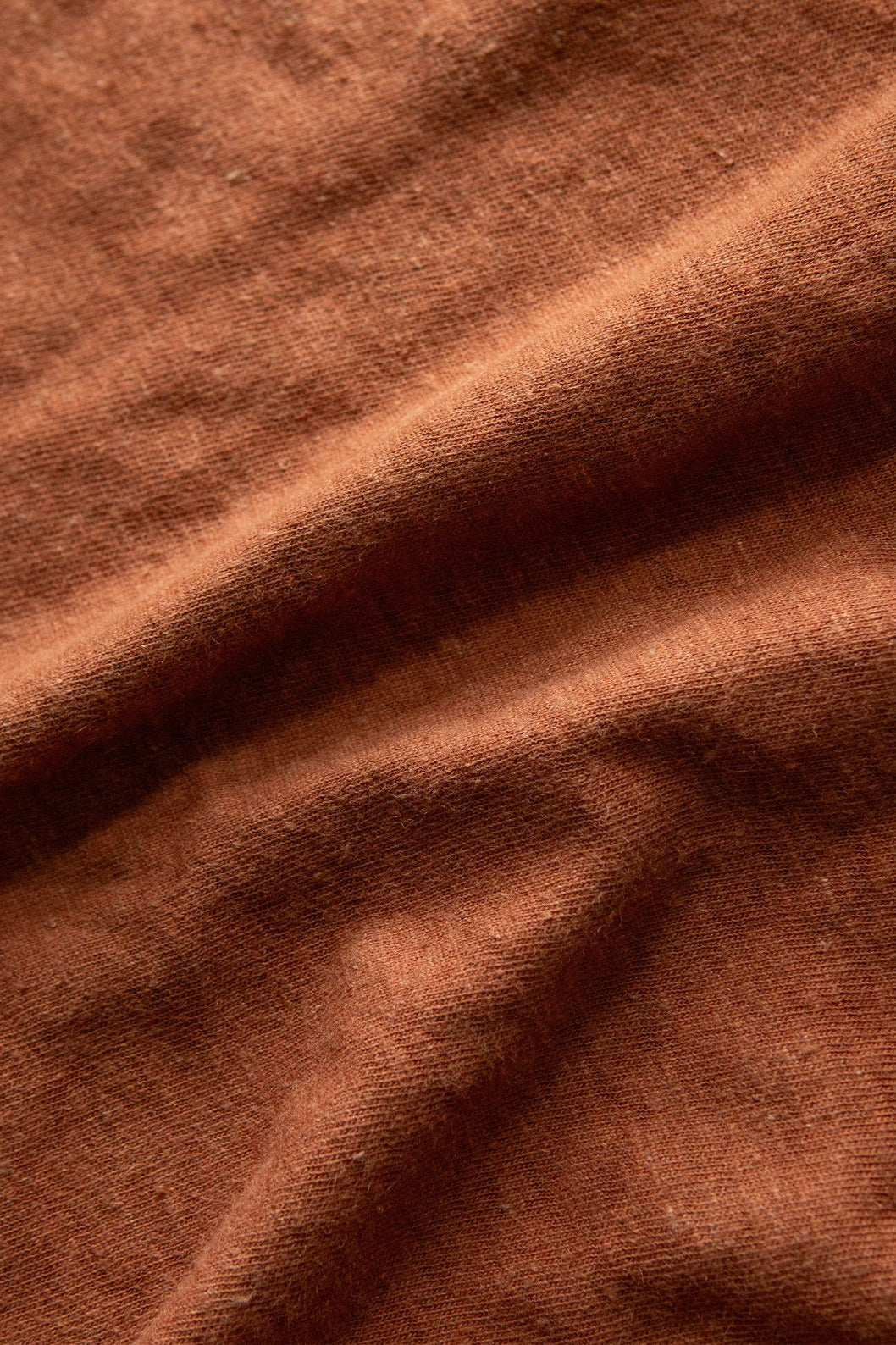 Close-up of the Bridge & Burn Organic Hemp Pocket Tee in Burnt Umber, showing the textured brown fabric with visible folds and soft, slightly fuzzy fibers.