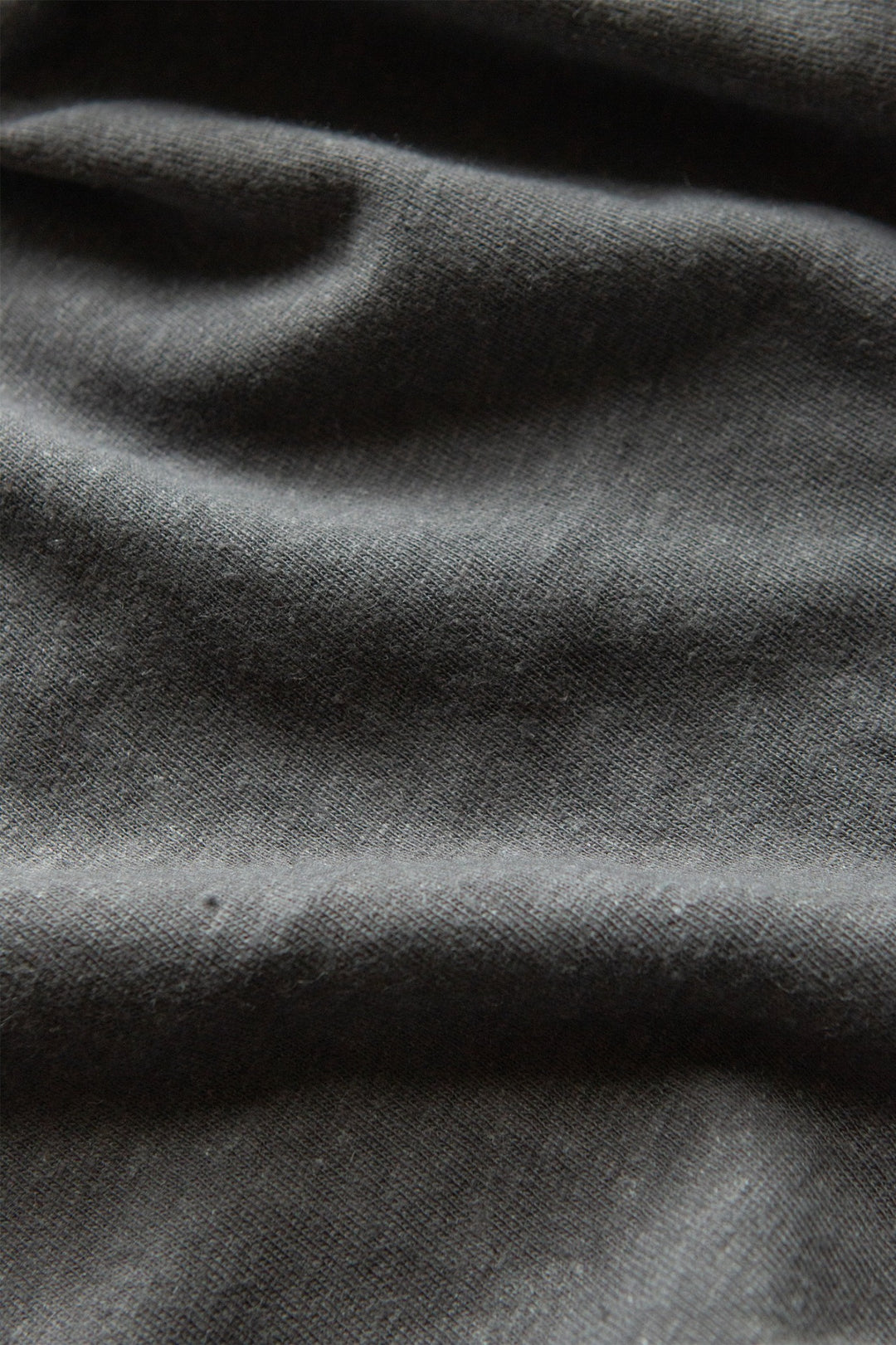 A close-up of the Organic Hemp Boxy Tee in Slate Grey by Bridge & Burn shows its textured dark gray fabric with gentle folds and subtle shadows, offering a soft look—perfect for a sustainable women's t-shirt.