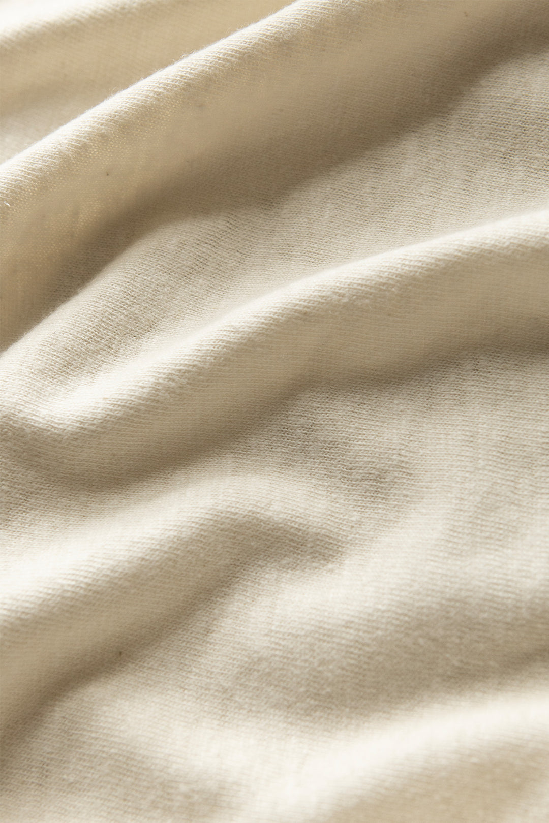 Close-up of the Organic Hemp Boxy Tee in Ivory by Bridge & Burn, featuring soft, cream-colored sustainable fabric with gentle folds and a subtly textured surface for warmth and comfort.