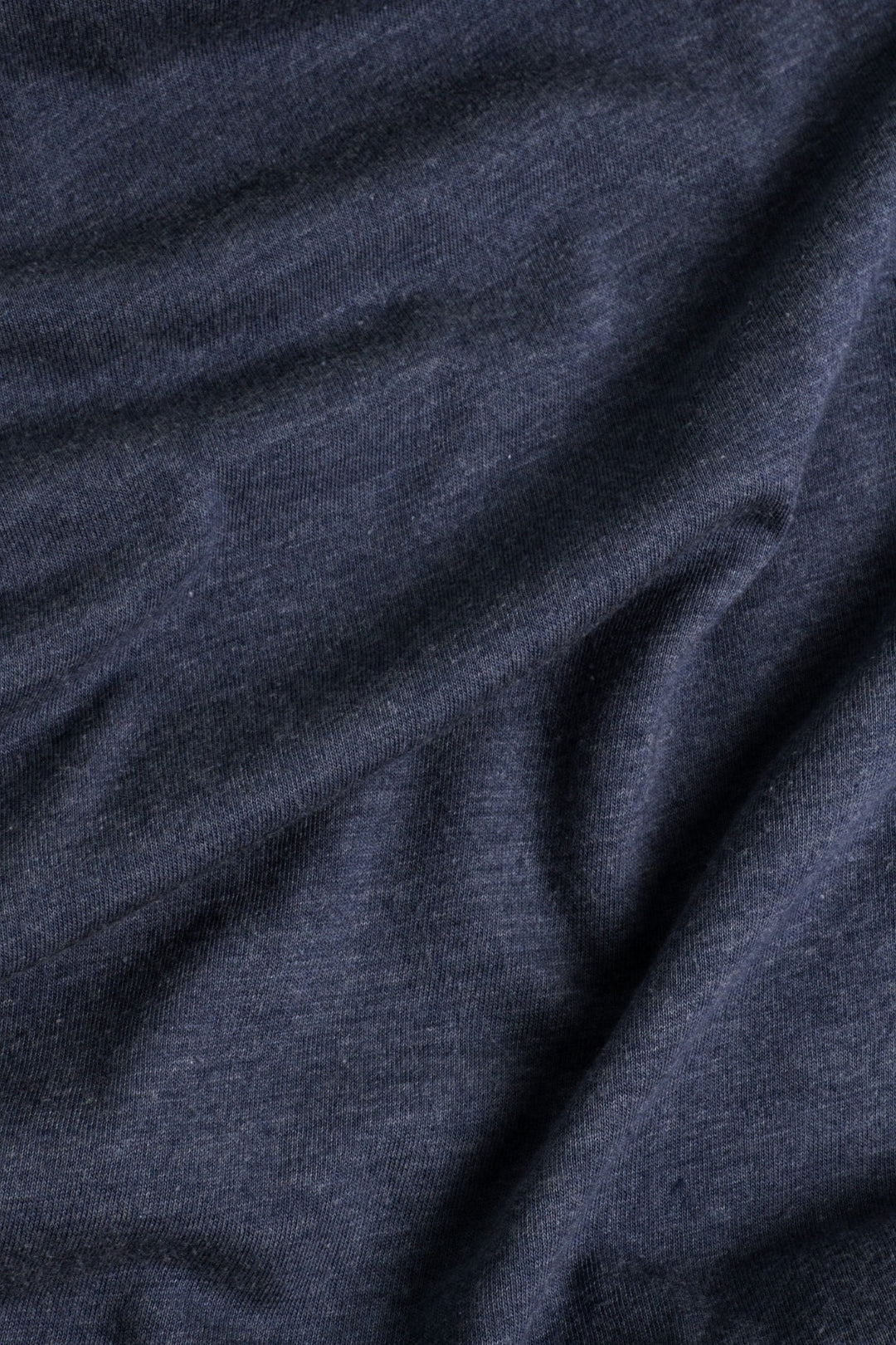 The Men's Alpenglow Tee by Bridge & Burn features eco-friendly navy fabric with a soft, slightly heathered texture and gentle, natural folds that create subtle shadows and highlights.