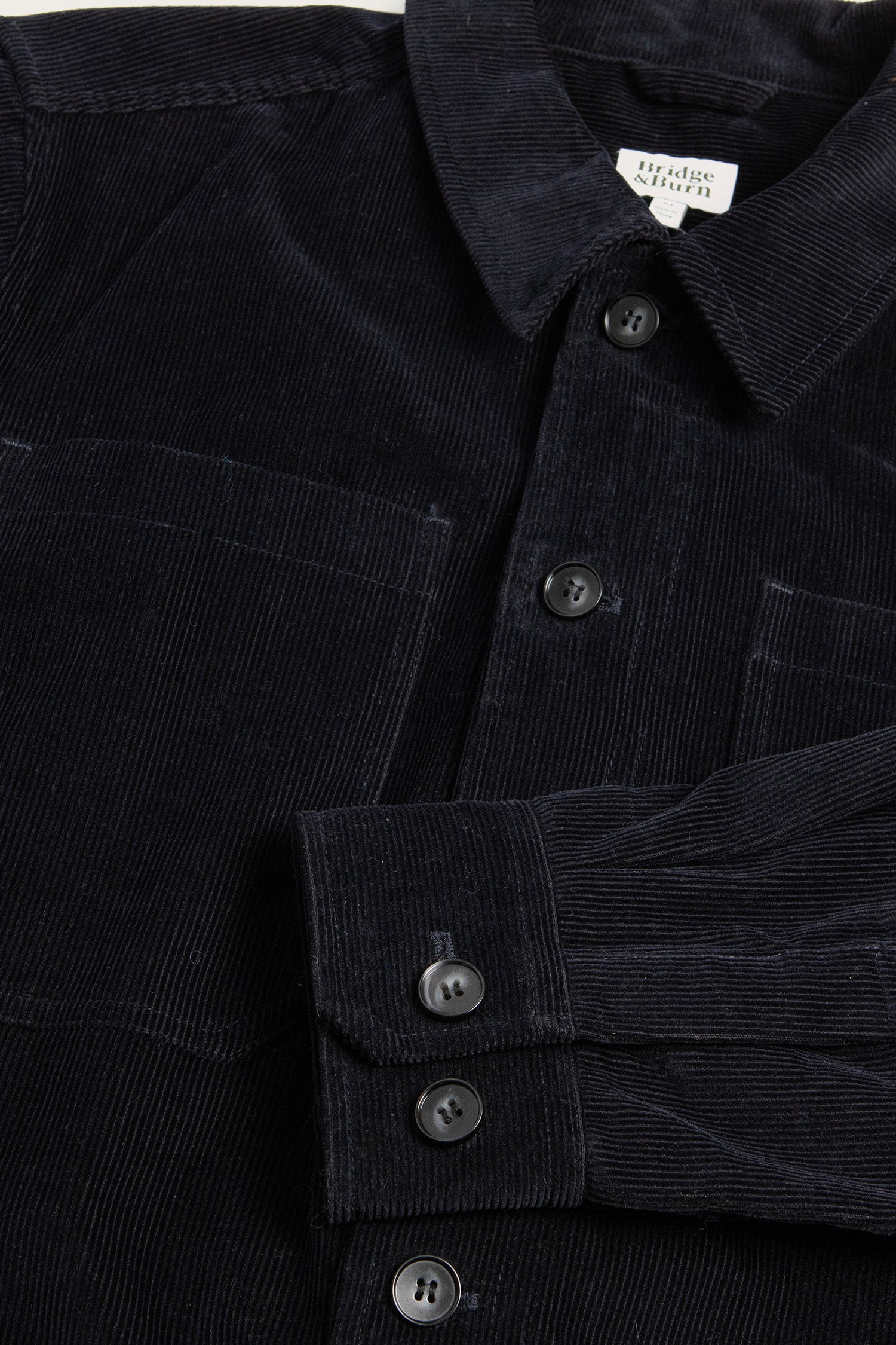 Close-up of the Banks Shirt Jacket by Bridge & Burn in Midnight Blue corduroy, featuring a collar, chest pocket, black buttons, and vertical ribbed texture—a soft yet sturdy workwear staple with a refined look.