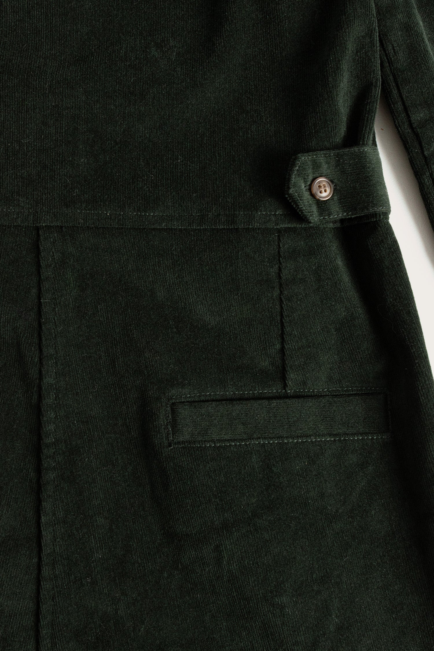 Close-up of the Bridge & Burn Faye Jumpsuit in Deep Pine Pinwale, showcasing a pocket, waistband with buttoned tab, and distinct vertical corduroy ridges.
