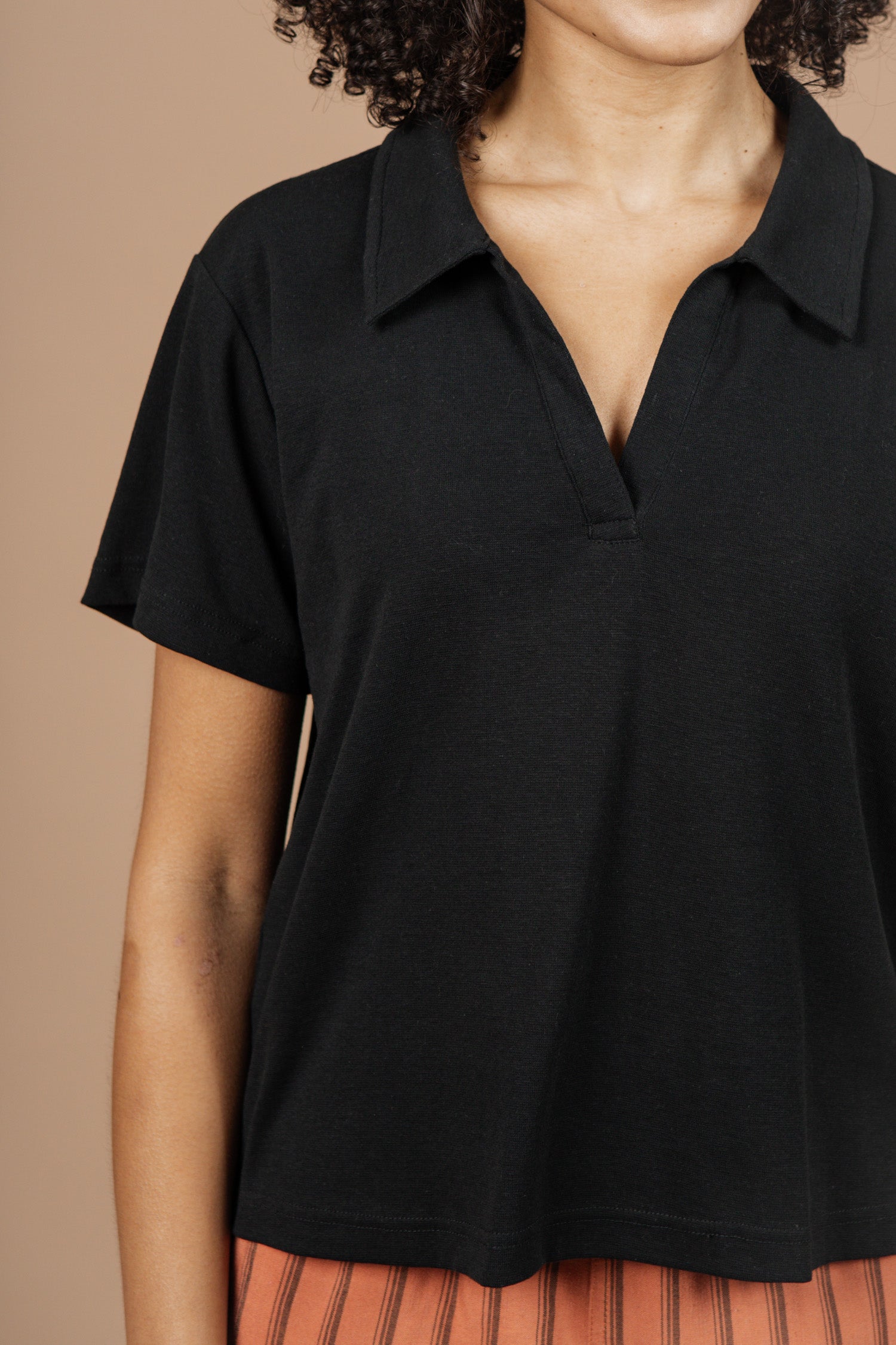 A person wearing the Bridge & Burn Avery Boxy Top in black jersey stands against a plain beige background. Their face is partially out of the frame, and they pair the top with orange striped pants.
