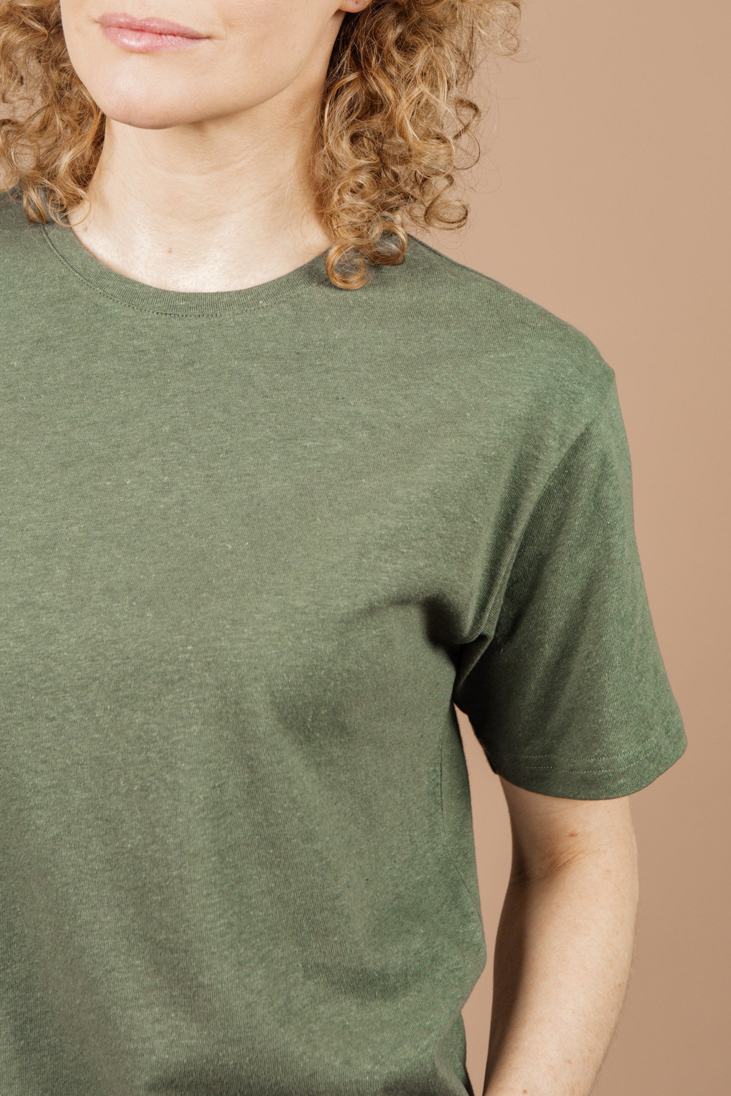 A person with curly blonde hair wears the Bridge & Burn Organic Hemp Boxy Tee in Cypress, shown from the shoulders up against a beige background.