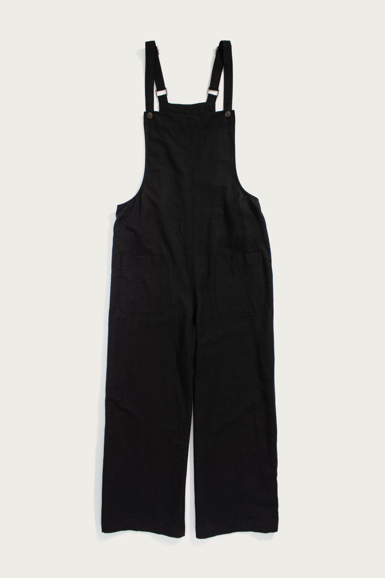 The Bridge & Burn Edie Overall in black, made from a soft tencel-cotton blend with wide legs, front patch pockets, and adjustable shoulder straps, is shown laid flat on a white background.