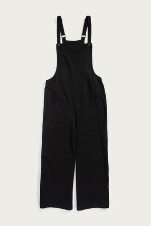 The Bridge & Burn Edie Overall in black, made from a soft tencel-cotton blend with wide legs, front patch pockets, and adjustable shoulder straps, is shown laid flat on a white background.