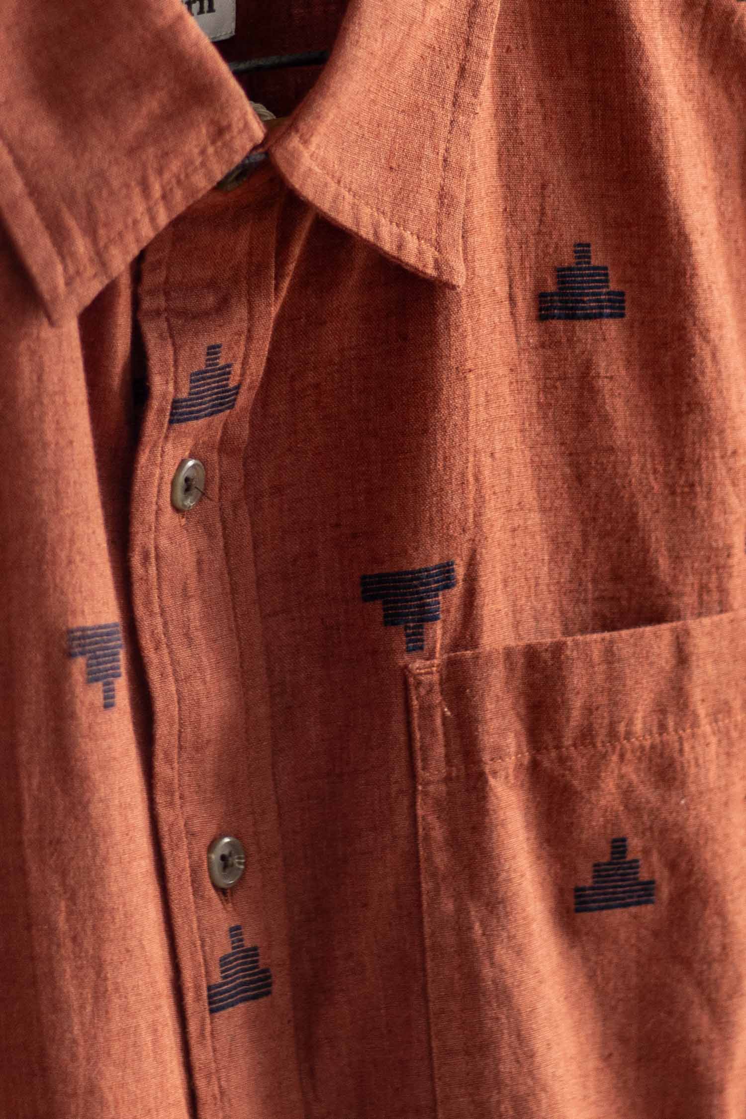 A close-up of the Bridge & Burn Malcolm Shirt in Rust Fil-Coupé Pyramids—a sustainable button-up with collar, chest pocket, and small navy geometric embroidery throughout the fabric.