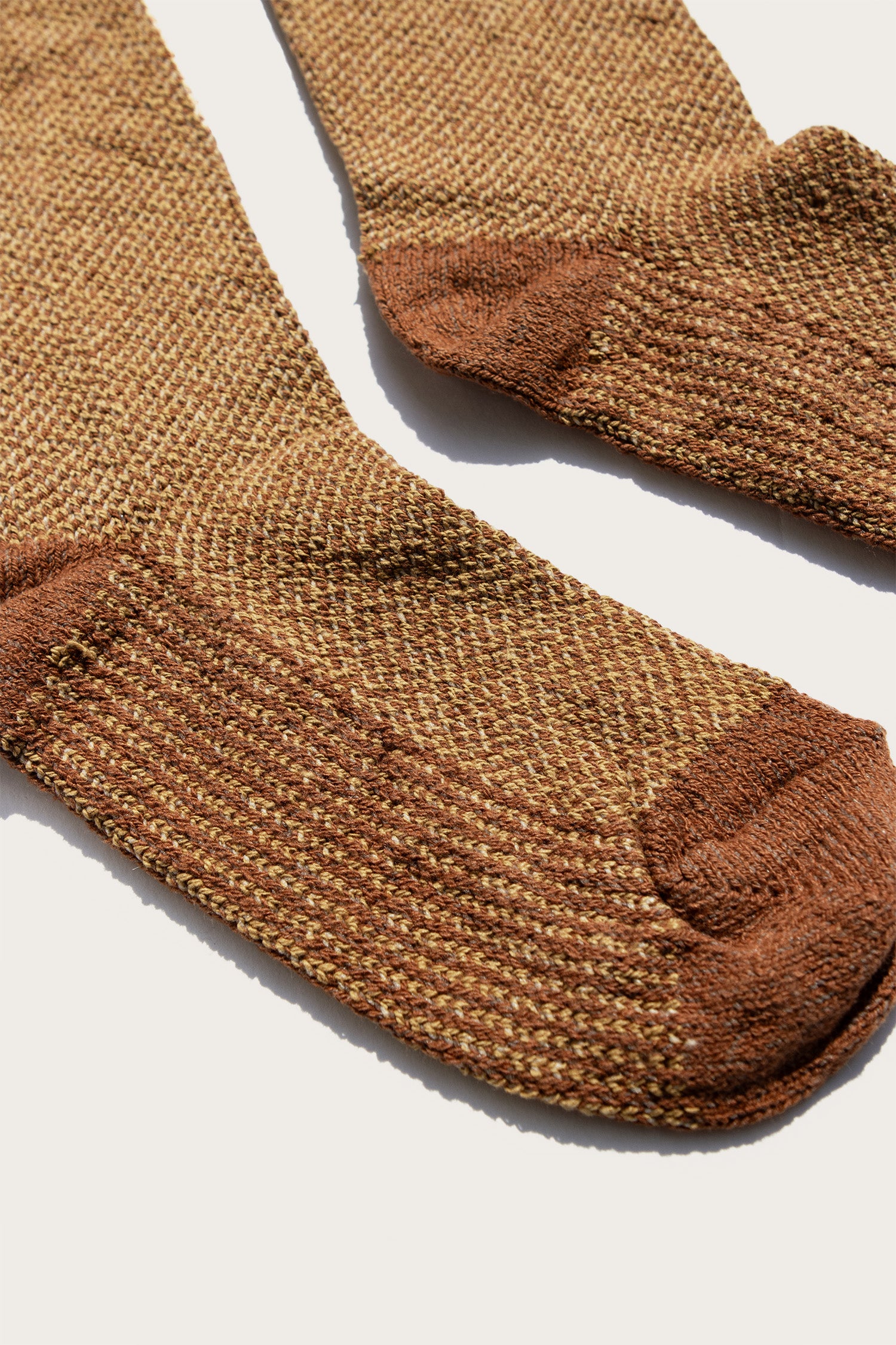 A close-up of the Bridge & Burn Helix Sock in Ochre, featuring textured brown and tan fabric with darker brown heel, toe, and cuff, laid flat on a light surface.