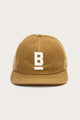 The Bridge & Burn B Flat Waxed Cap in brown features British Millerain waxed canvas, a flat brim, and a white embroidered underlined 