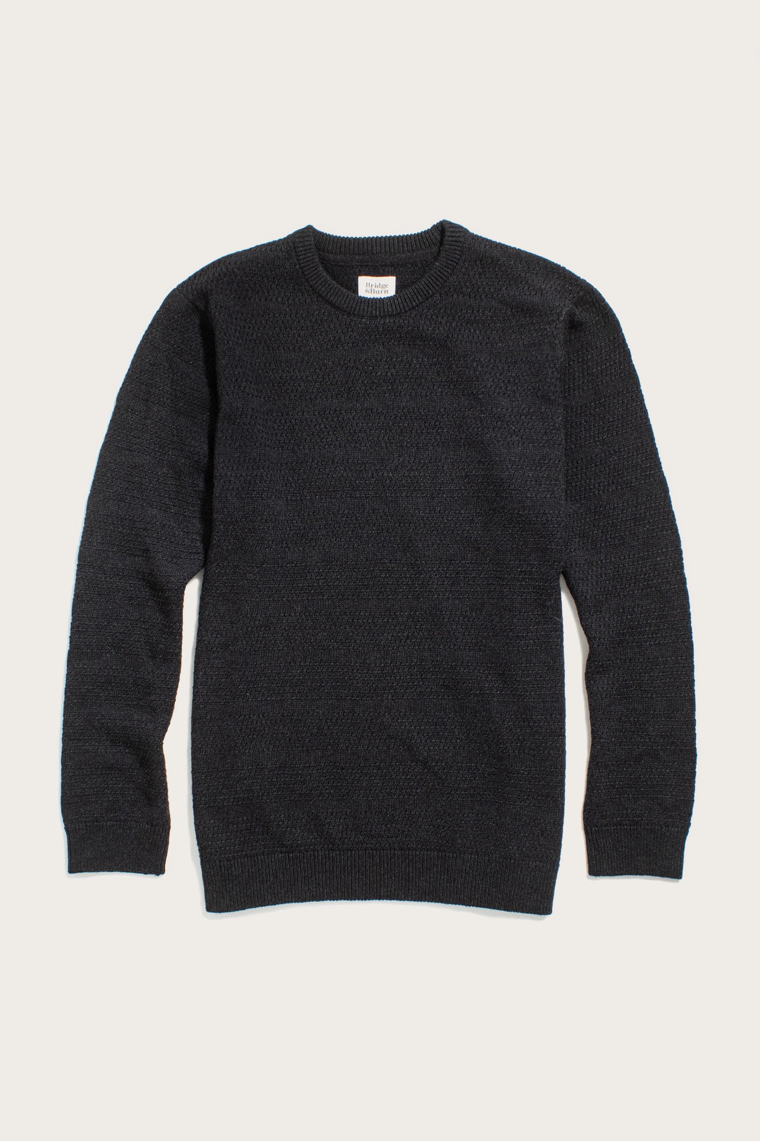 The Bridge & Burn Calder Sweater in Midnight is a long-sleeve crew neck sustainable knit, shown laid flat on a light background, with textured stitching and ribbed cuffs, collar, and hem.