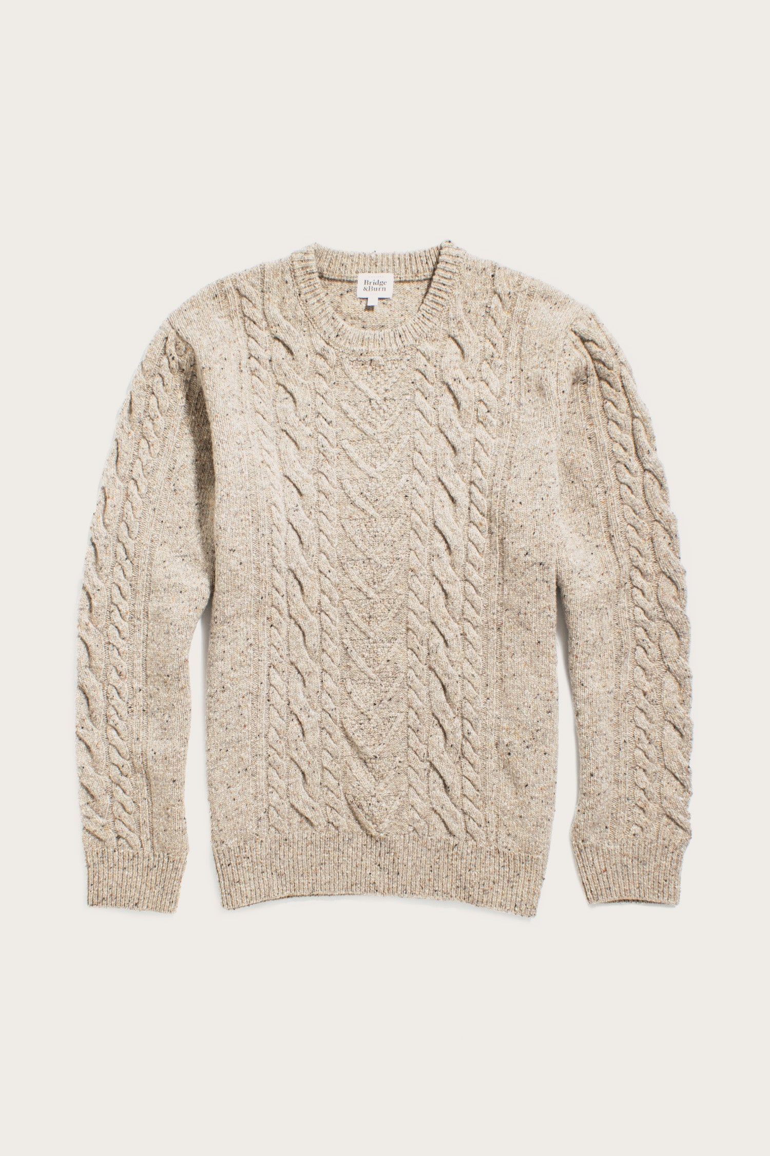 The Bridge & Burn Ludlow Sweater in Flecked Oatmeal is a beige cable-knit sweater made from RWS-certified wool, with a crew neck plus ribbed cuffs and hem. Shown laid flat on a plain white background.
