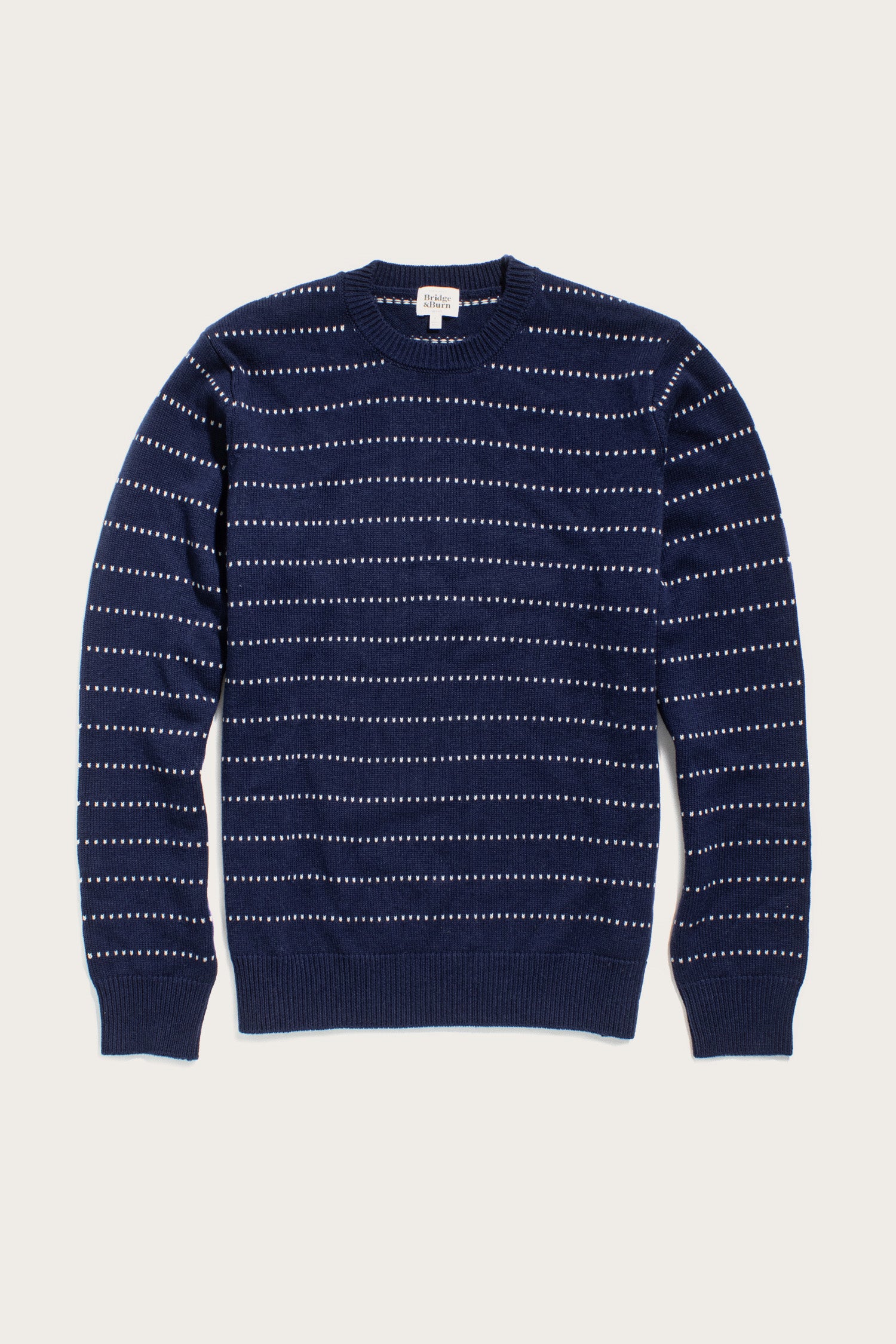 The Orson Sweater in Navy Dotted Path by Bridge & Burn is a lightweight merino wool crewneck featuring thin, evenly spaced white dashed lines and ribbed trim—perfect for sustainable wardrobes.