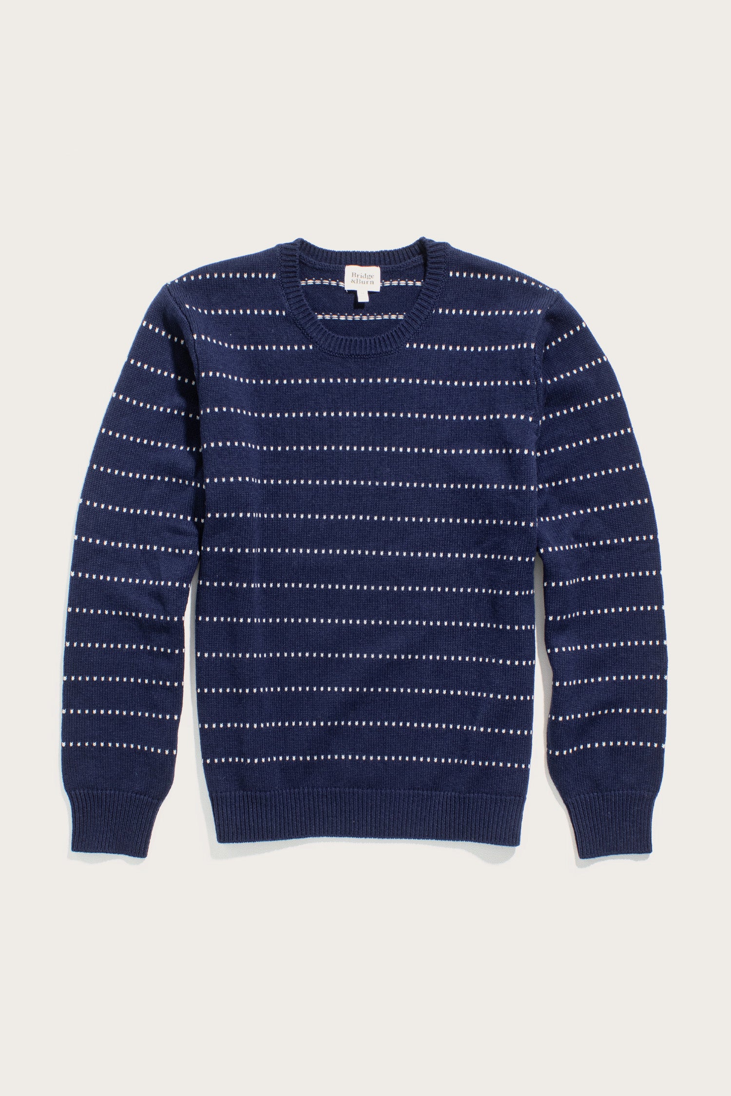 The Bridge & Burn Cline Sweater in Navy Dotted Path is a lightweight, long-sleeved crew neck featuring evenly spaced horizontal white dashed lines.