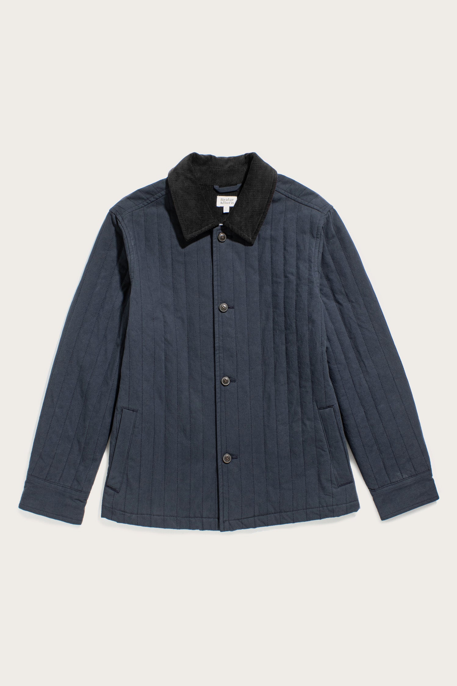 The Bridge & Burn Kenton Jacket in Slate features a lightweight quilted design, corduroy collar, button-down front, two side pockets, and long sleeves, shown laid flat on a light background.