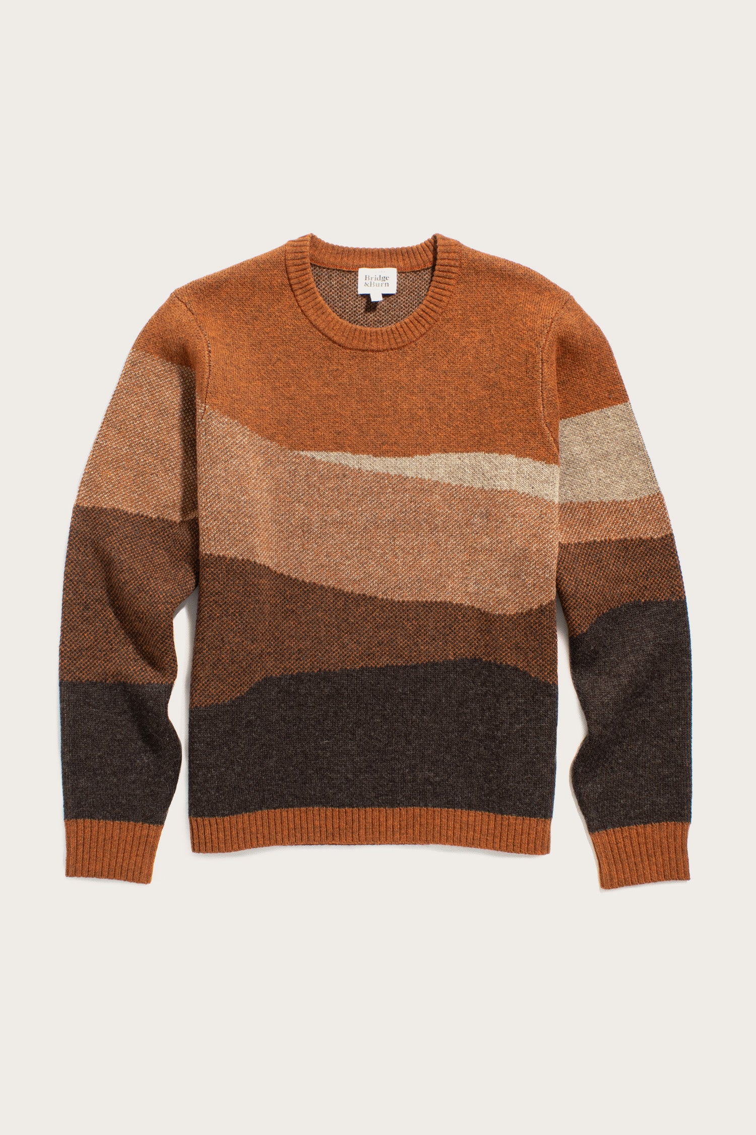 The Bridge & Burn Petra Sweater in Sandstone is a knit merino wool crewneck with long sleeves, showcasing horizontal wave stripes in rust, brown, beige, and dark gray.