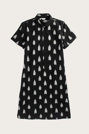 The Delia Shirt Dress in Eclipse Ikat by Bridge & Burn is a knee-length, black organic cotton dress with short sleeves, a collar, front buttons, and an allover white ikat pattern.