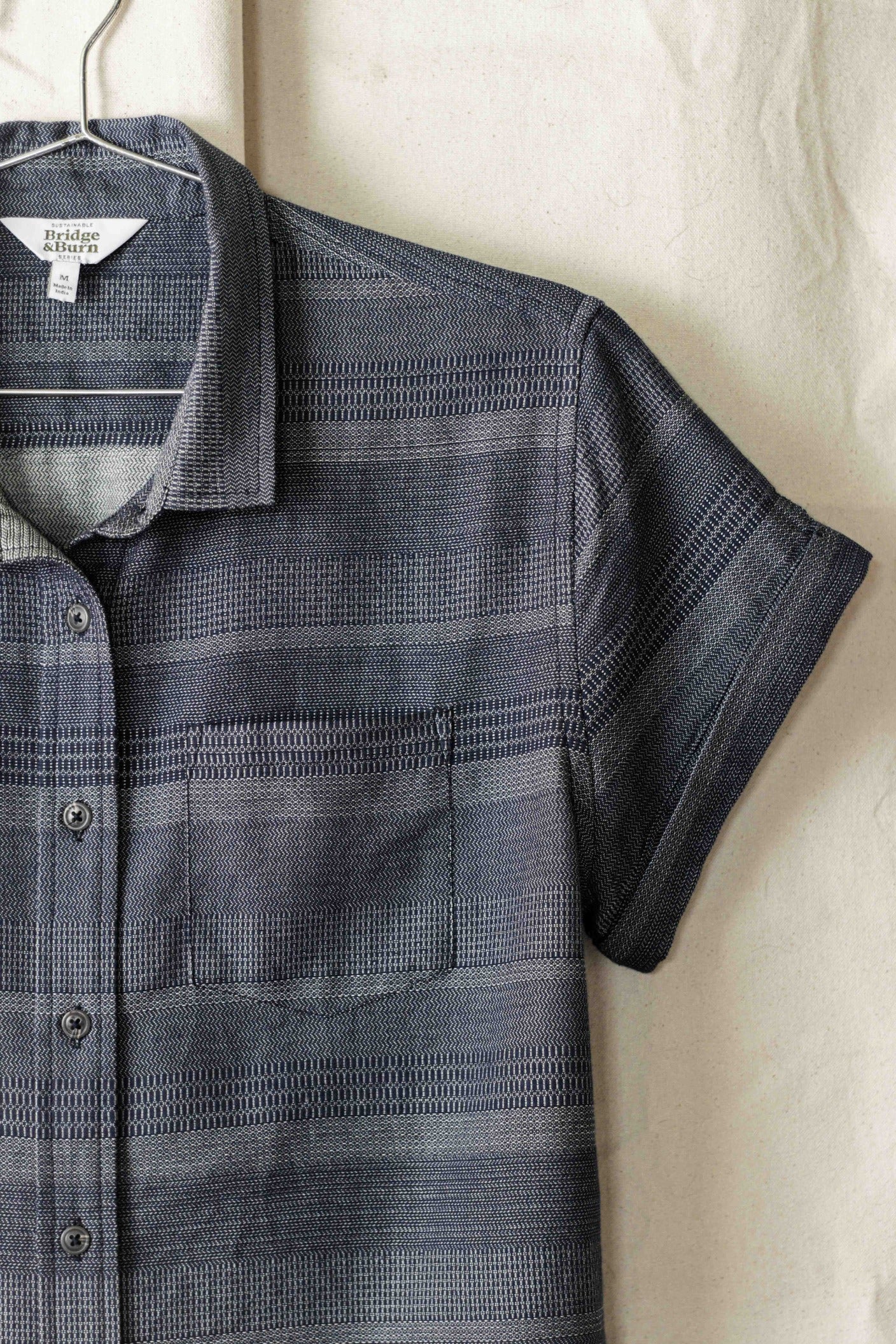 The Bea Shirt / Cascade Weave by Bridge & Burn, a tailored-fit short-sleeve button down with gray and navy horizontal stripes, features a collar, chest pocket, and is made from soft organic cotton for comfort.