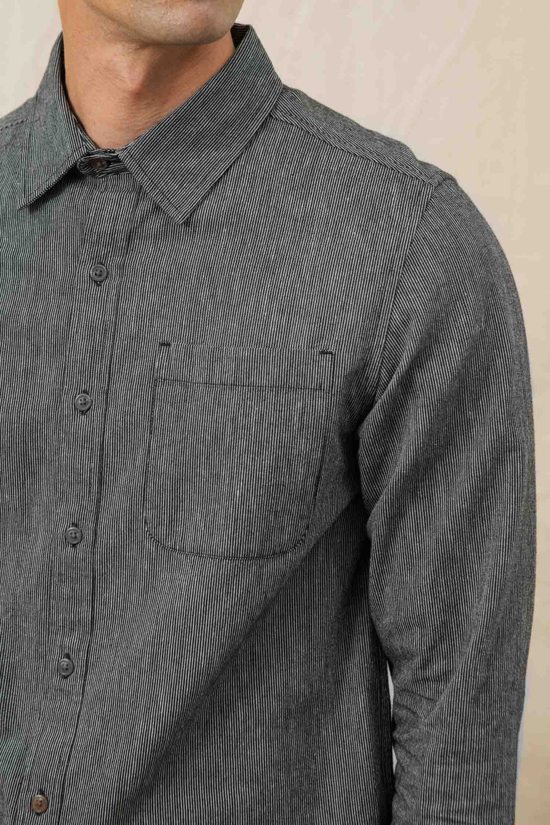 A close-up shows a person wearing the Bridge & Burn Jude Shirt in Onyx Stripe—men's, gray pinstripe, 100% cotton, with long sleeves and a small chest pocket. Only the torso and lower face are visible.