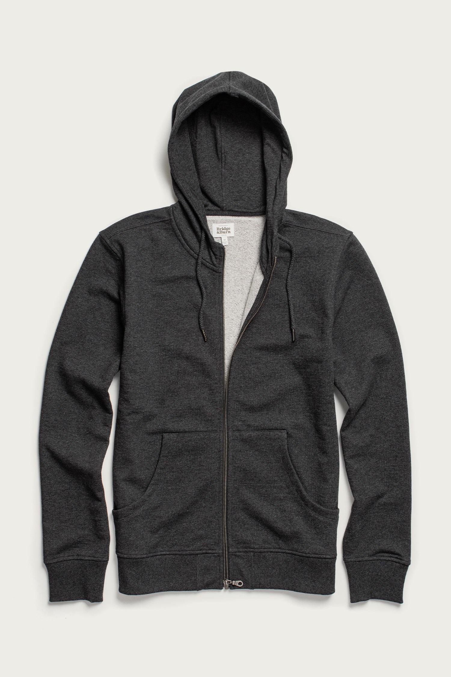 The Ridge Hoodie in Graphite by Bridge & Burn is a zip-up hoodie made from soft organic cotton, featuring a classic hood for comfort.