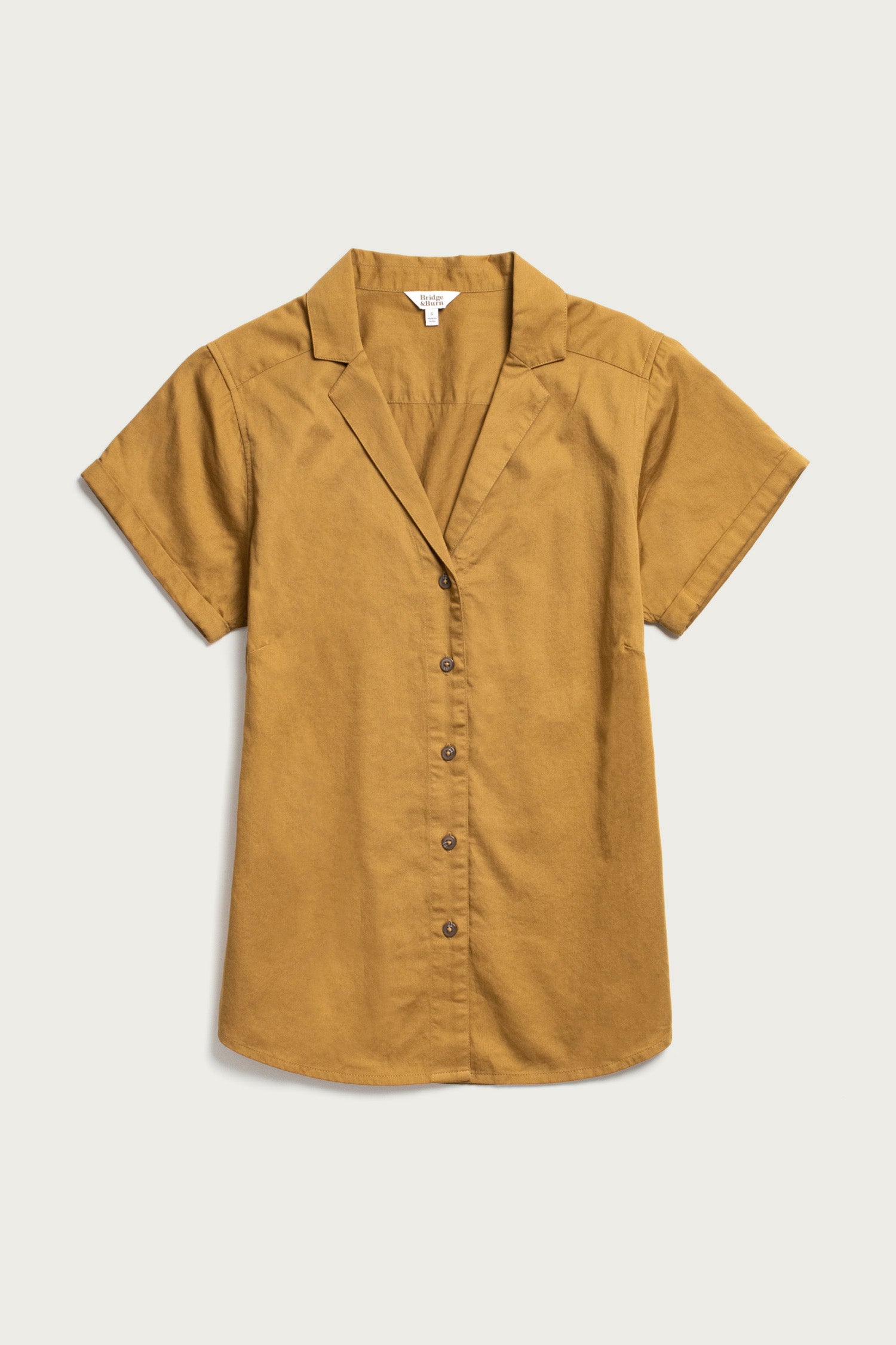 The Bridge & Burn Innes Shirt in Gold is a short-sleeve, relaxed-fit button-up with a notched collar, laid flat on a light background for effortless style.