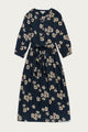 The Bridge & Burn Fiona Dress / Night Garden is a long-sleeved midi dress featuring a white and beige floral pattern, gathered sleeves, round neckline, and waist tie, shown laid flat on a light background.