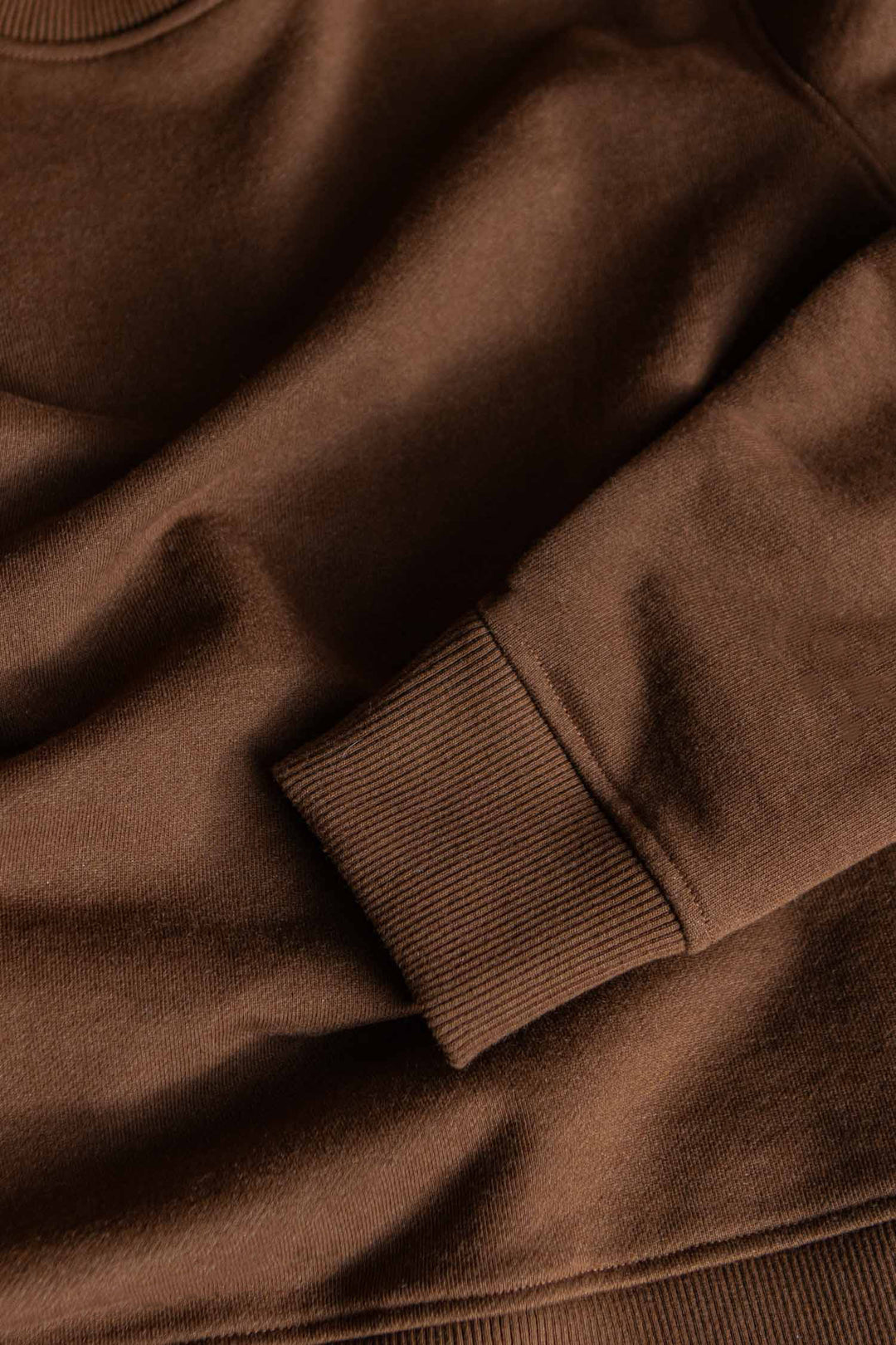 A close-up of the Bridge & Burn Hayden Crew Sweatshirt in Cumin, highlighting the ribbed cuff of one sleeve and the smooth, soft texture of its recycled cotton fabric on this timeless crew neck pullover.