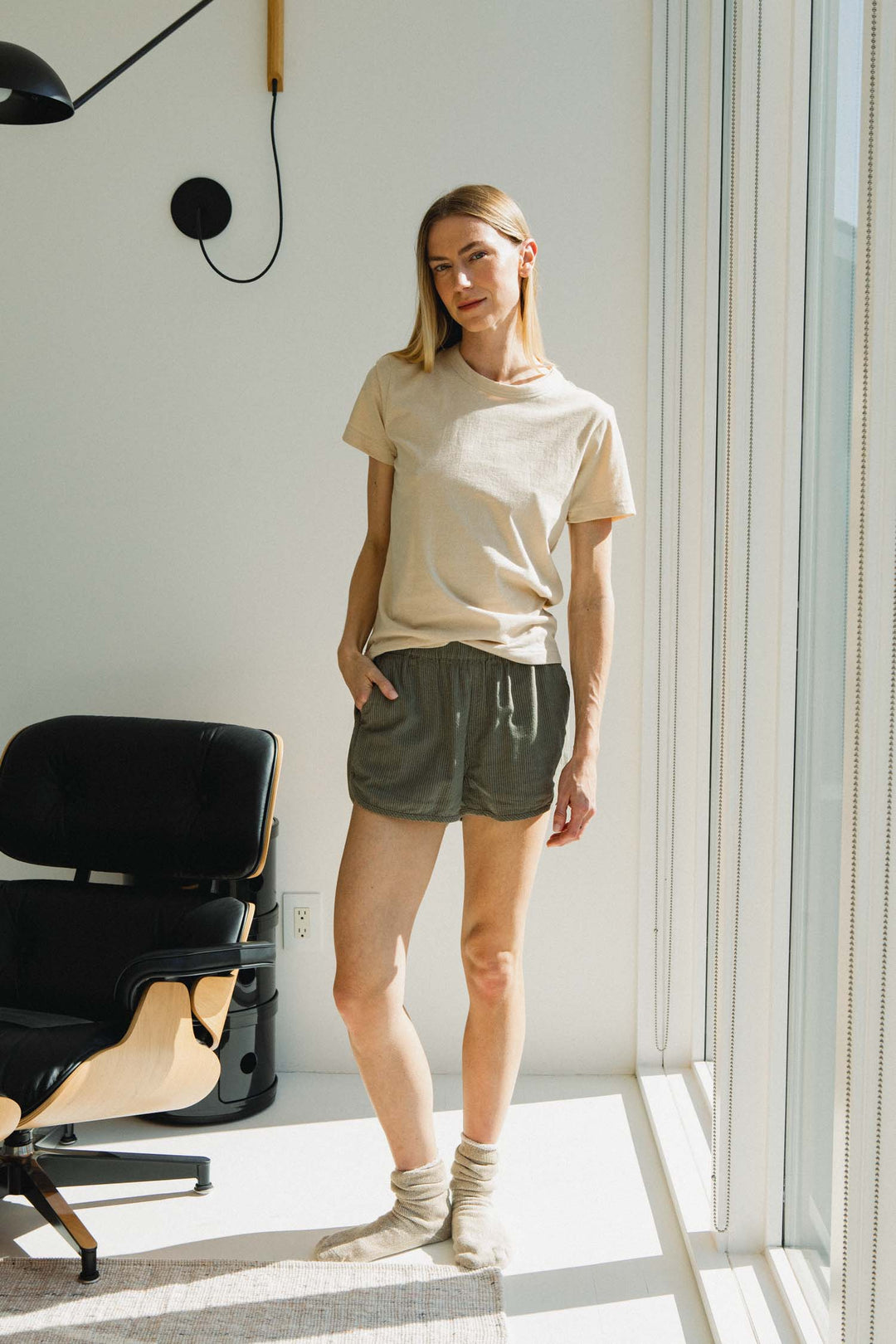 A woman wearing a tan t-shirt and Luca Track Short / Olive Pinstripe shorts.