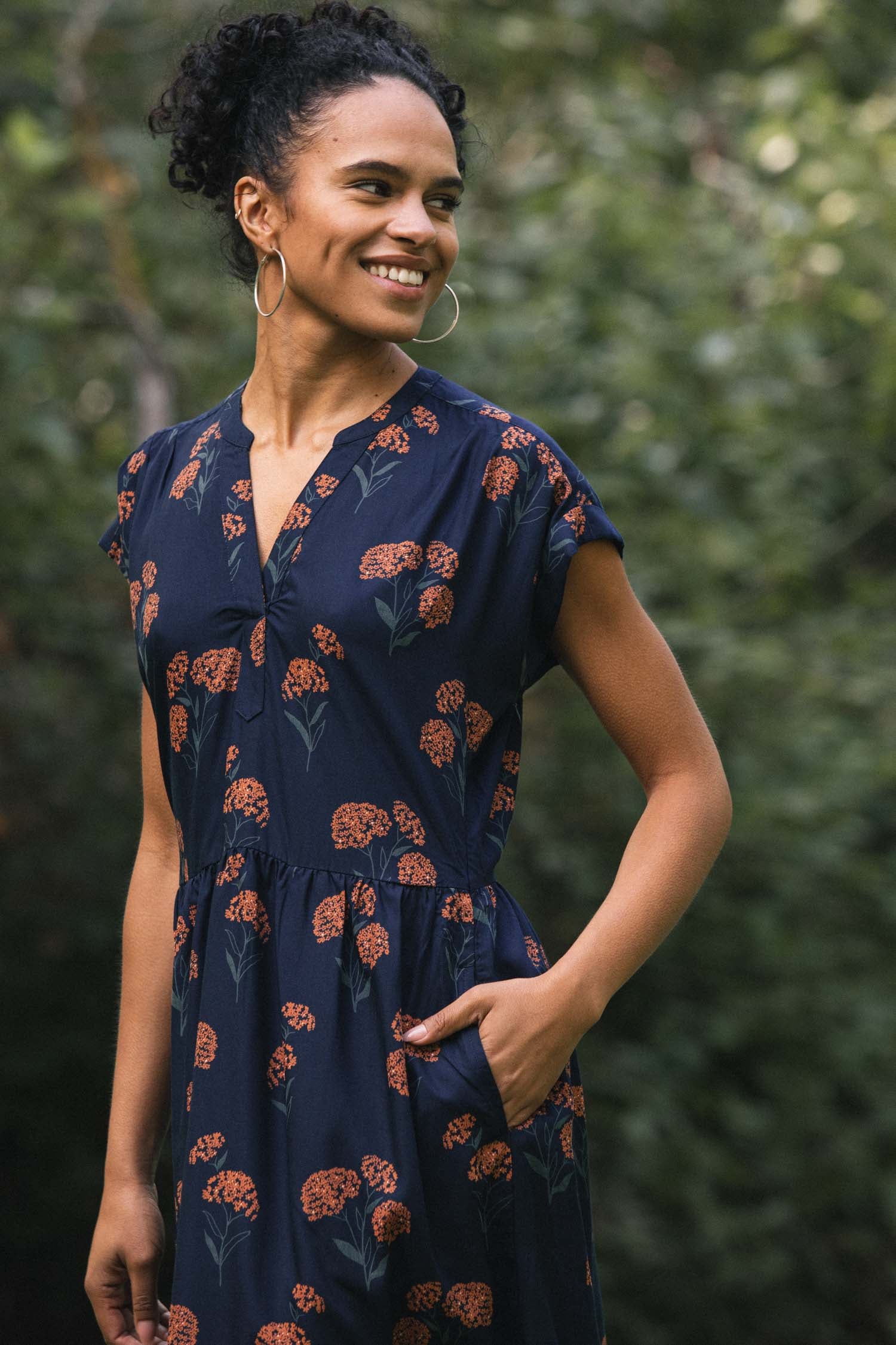 The Bridge & Burn Ira Dress / Wildflower is a navy blue knee-length modal pullover with short sleeves, a V-neckline, an elastic waist, and an orange and green floral print. Shown laid flat on a white background.