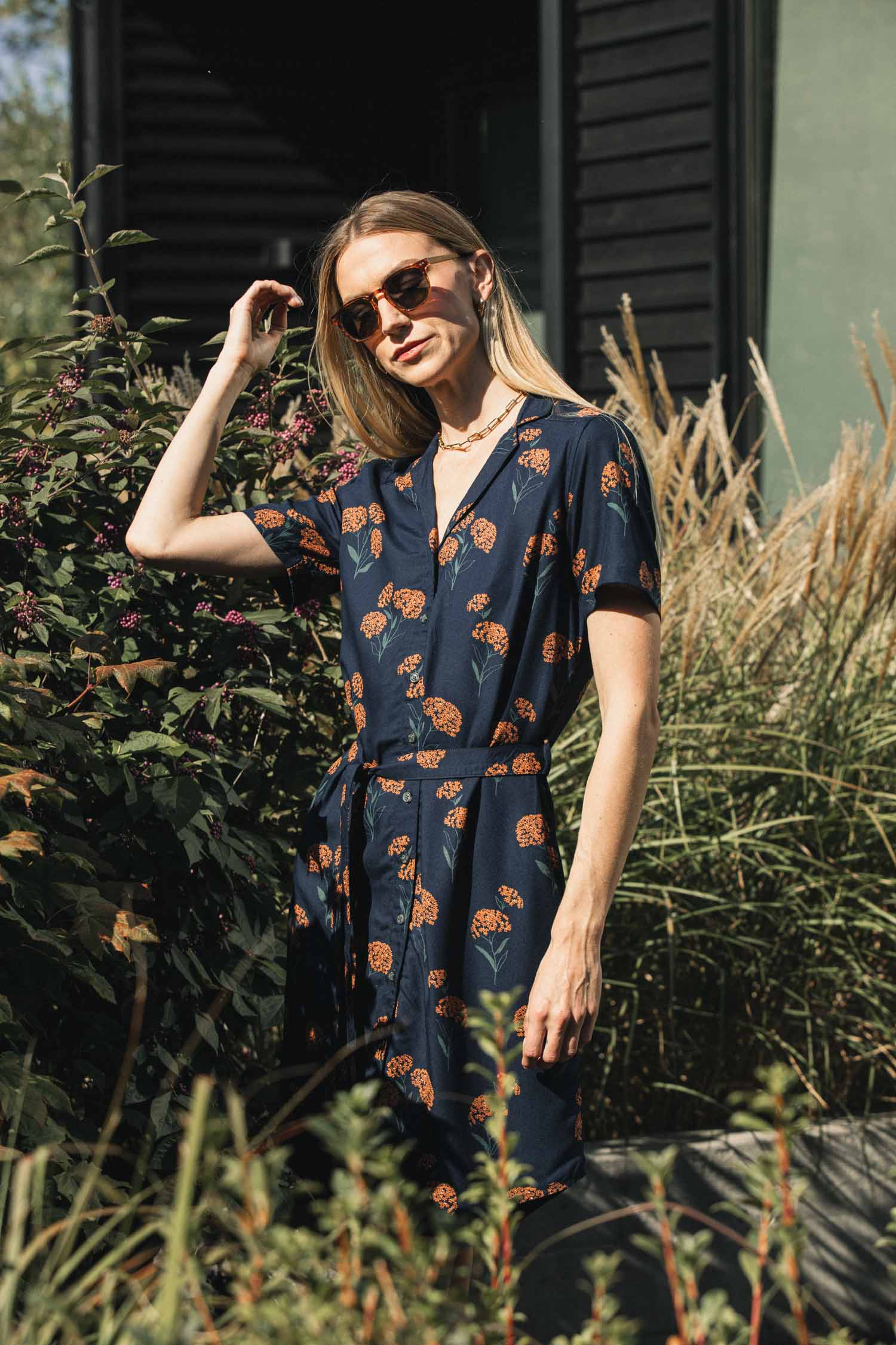 A woman wearing the Bridge & Burn Sofia Shirt Dress / Wildflower, a sustainable dark blue modal dress with a short-sleeved button-down design, orange wildflower print, and matching self-belted waist.