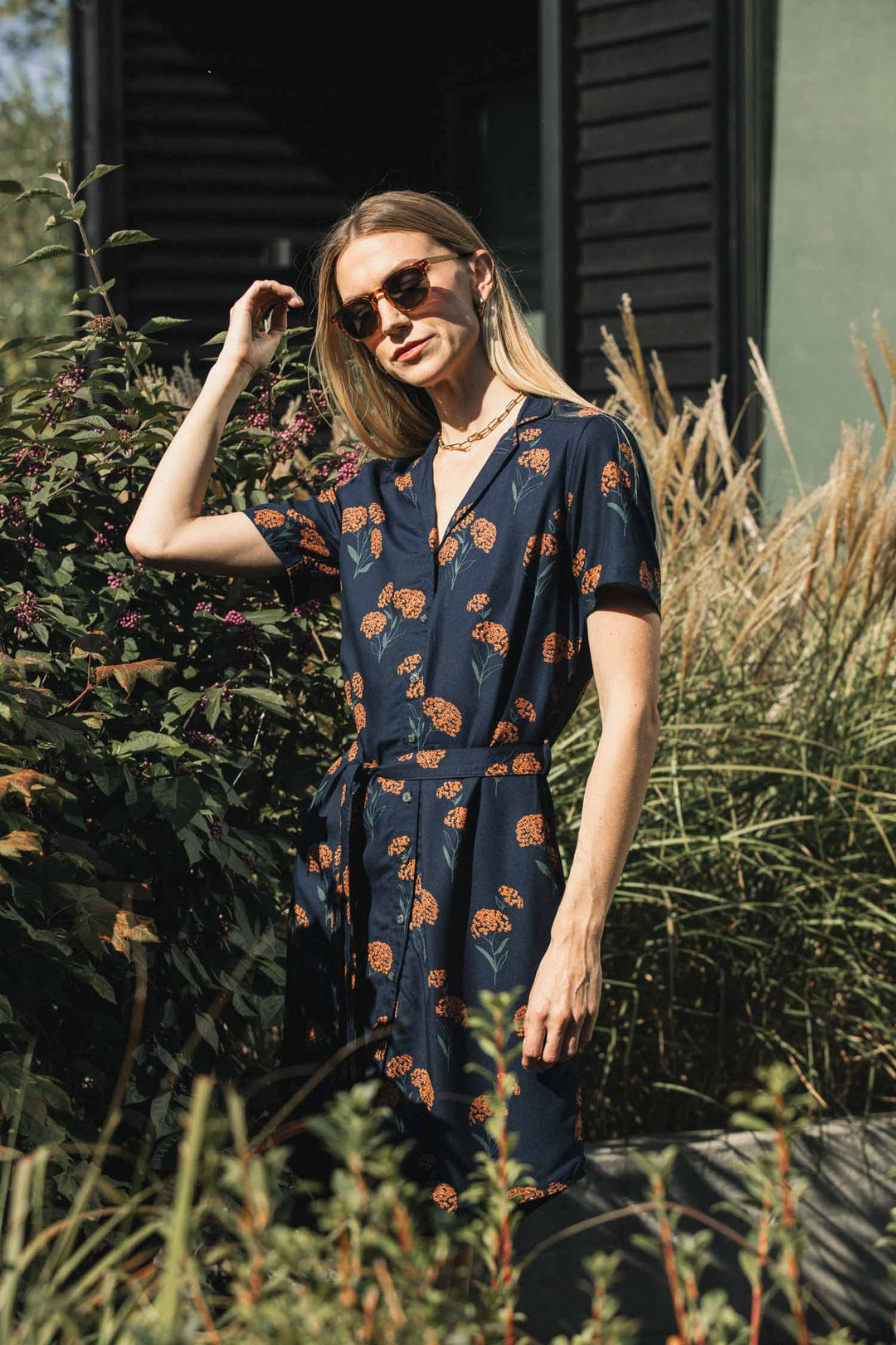 A woman wearing the Bridge & Burn Sofia Shirt Dress / Wildflower, a sustainable dark blue modal dress with a short-sleeved button-down design, orange wildflower print, and matching self-belted waist.