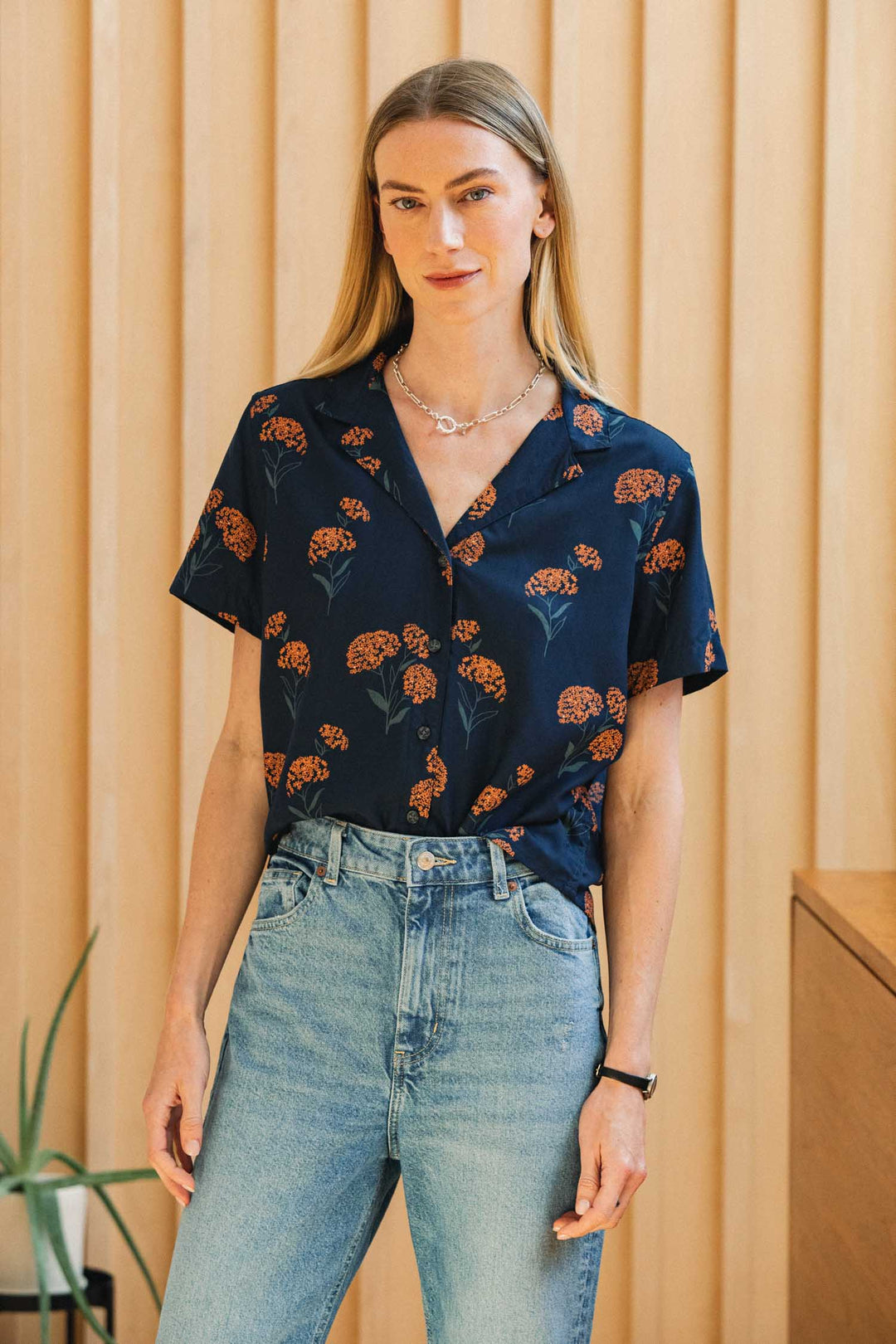 A person wearing a navy blue Bridge & Burn Mila Cropped Shirt / Wildflower with an orange wildflower print and light-wash blue jeans.