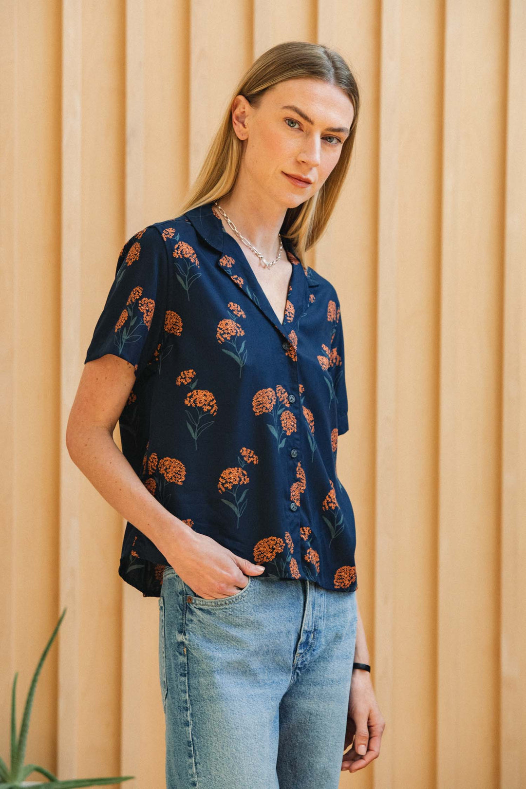 A person wears a navy blue Bridge & Burn Mila Cropped Shirt / Wildflower with an orange wildflower print and light-wash blue jeans.