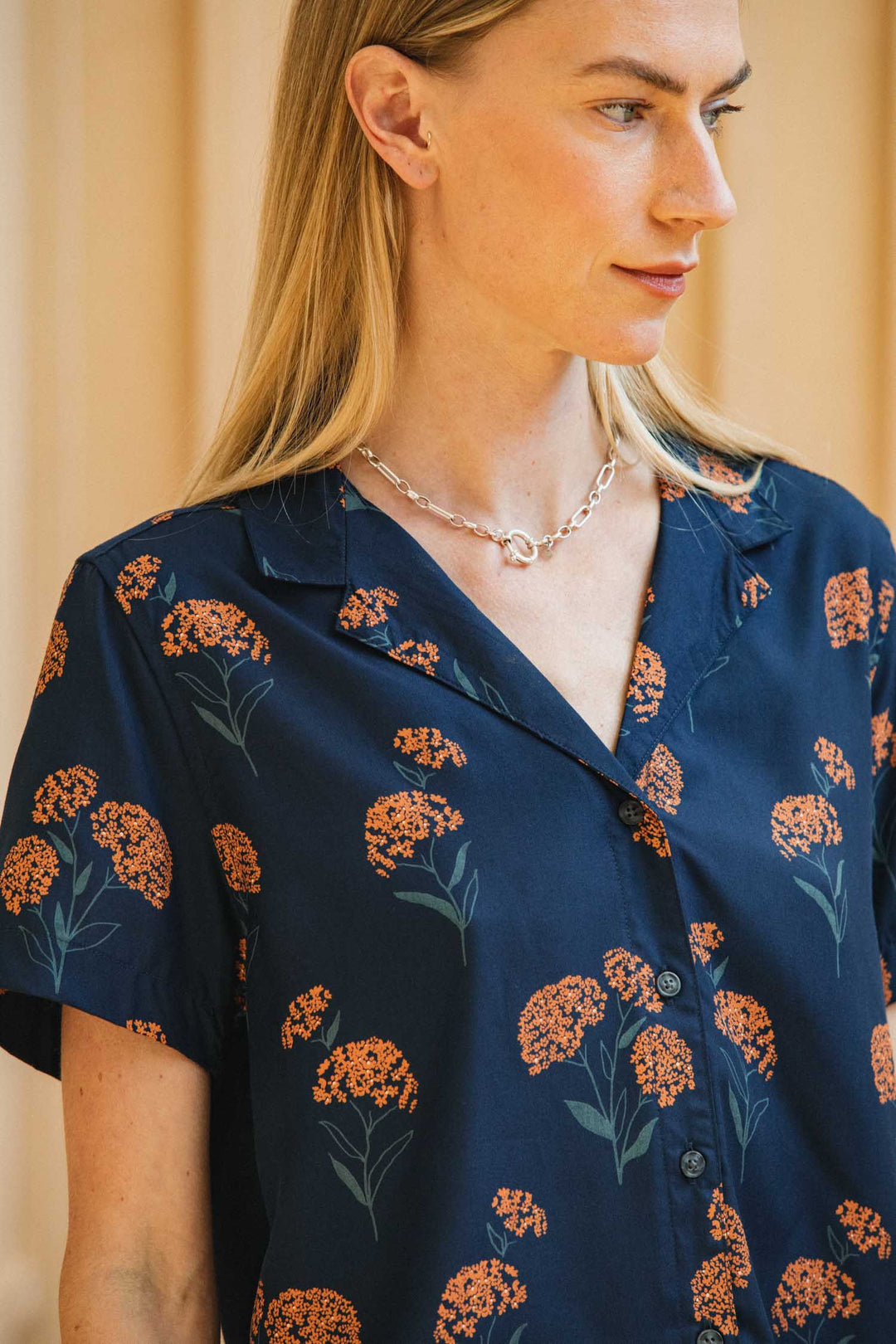 A person wears a dark blue, cropped Mila Cropped Shirt / Wildflower, featuring a short-sleeved collared design with an orange wildflower print.