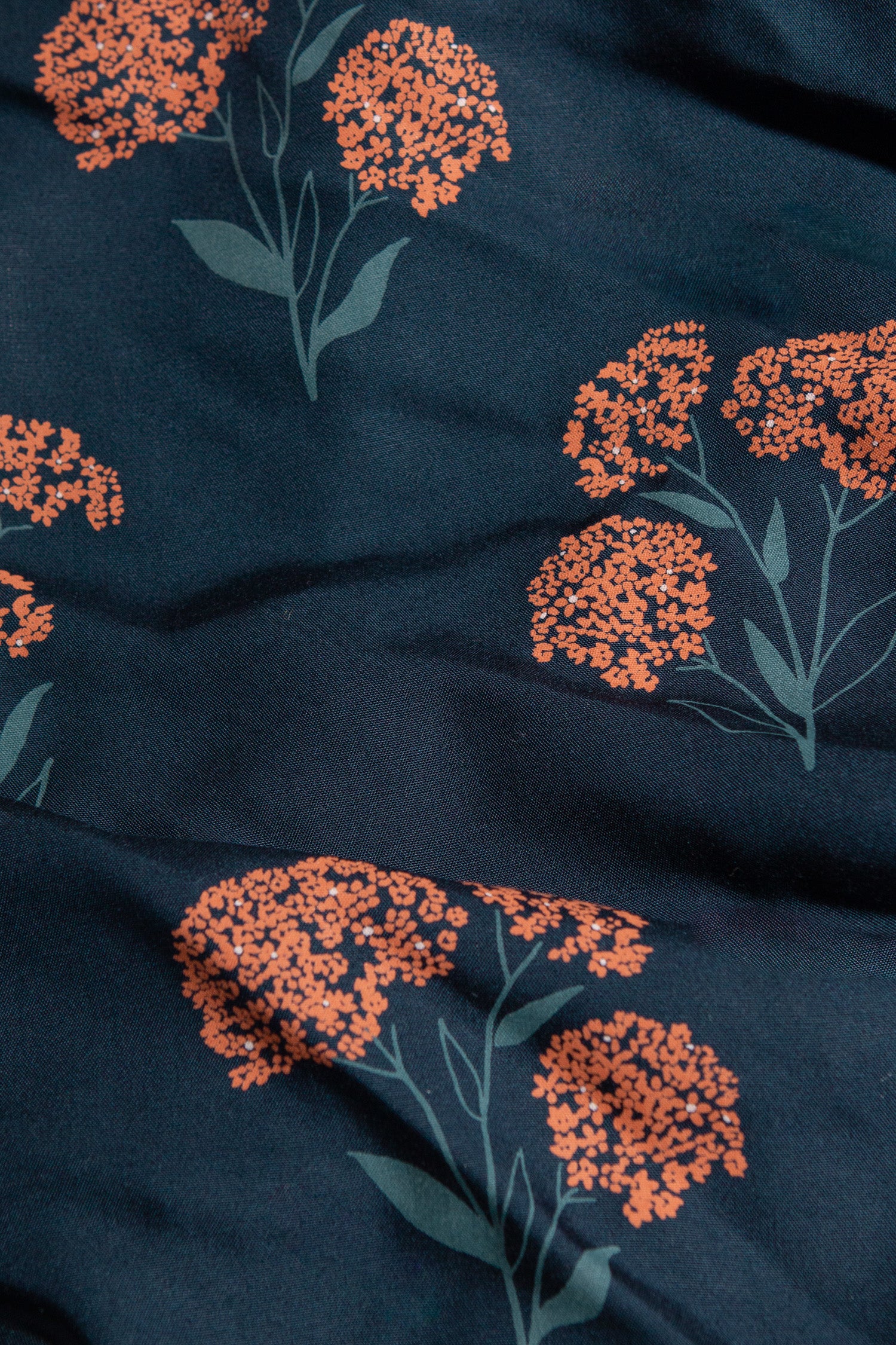 A close-up of the Mila Cropped Shirt / Wildflower by Bridge & Burn, showing dark blue sustainable fabric with orange floral clusters and green stems.