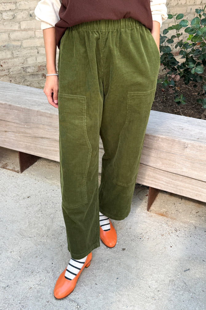 Le Bon Shoppe Gardener’s Pant in Bay Leaf corduroy, a relaxed fit style with large patch pockets, worn with black and white striped socks and orange flats.