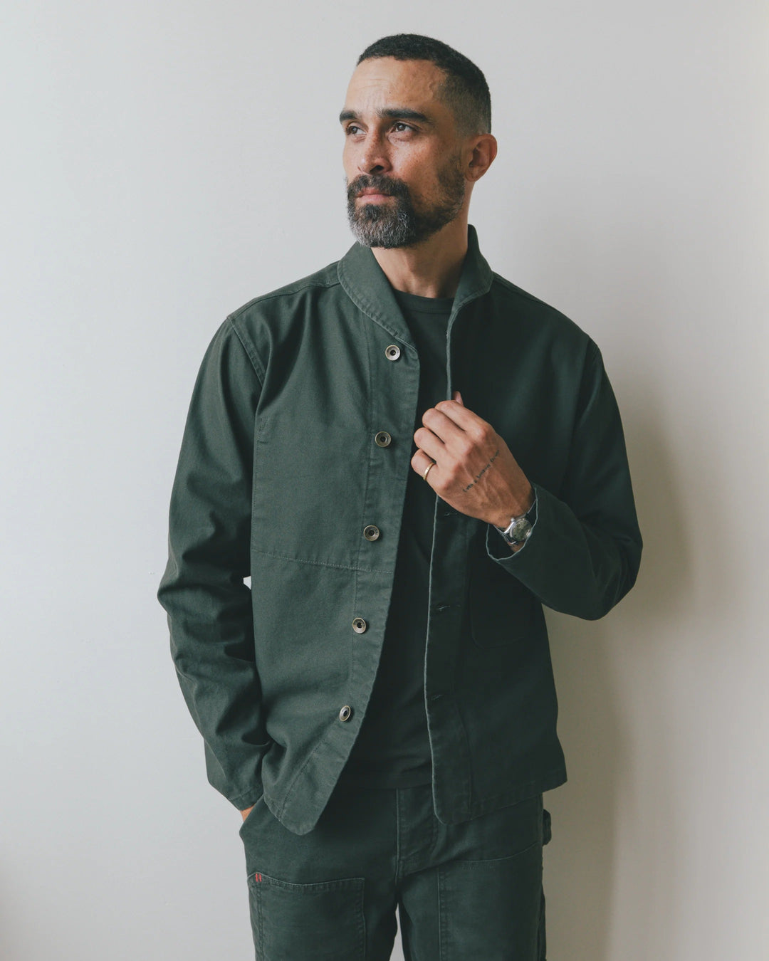 A bearded man wears an Imperfects - Shepherds Shirt Craft Canvas / Greenroom in dark green over a matching t-shirt.