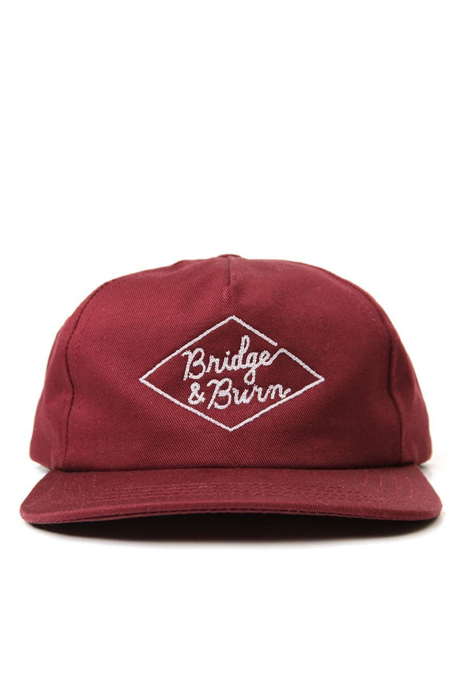 The Bridge & Burn Diamond Head Cap in burgundy is a maroon baseball hat made from durable cotton twill, showcasing white embroidered “Bridge & Burn” text within a diamond-shaped outline on the front. This pinch front cap is completed with a leather strap at the back for adjustable comfort.